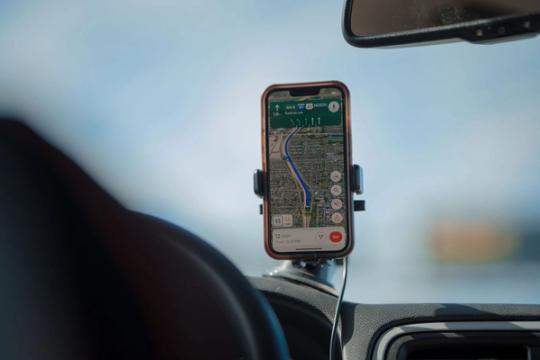 A smartphone with GPS navigation app mounted on a car dashboard during a road trip.