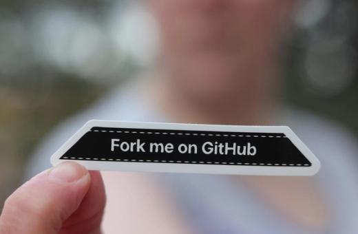Ranka laiko GitHub lipduką ant nešiojamojo kompiuterio