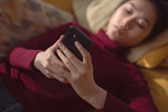 Moteris ilsėdamasi naudojasi telefonu, asociatyvi nuotrauka.