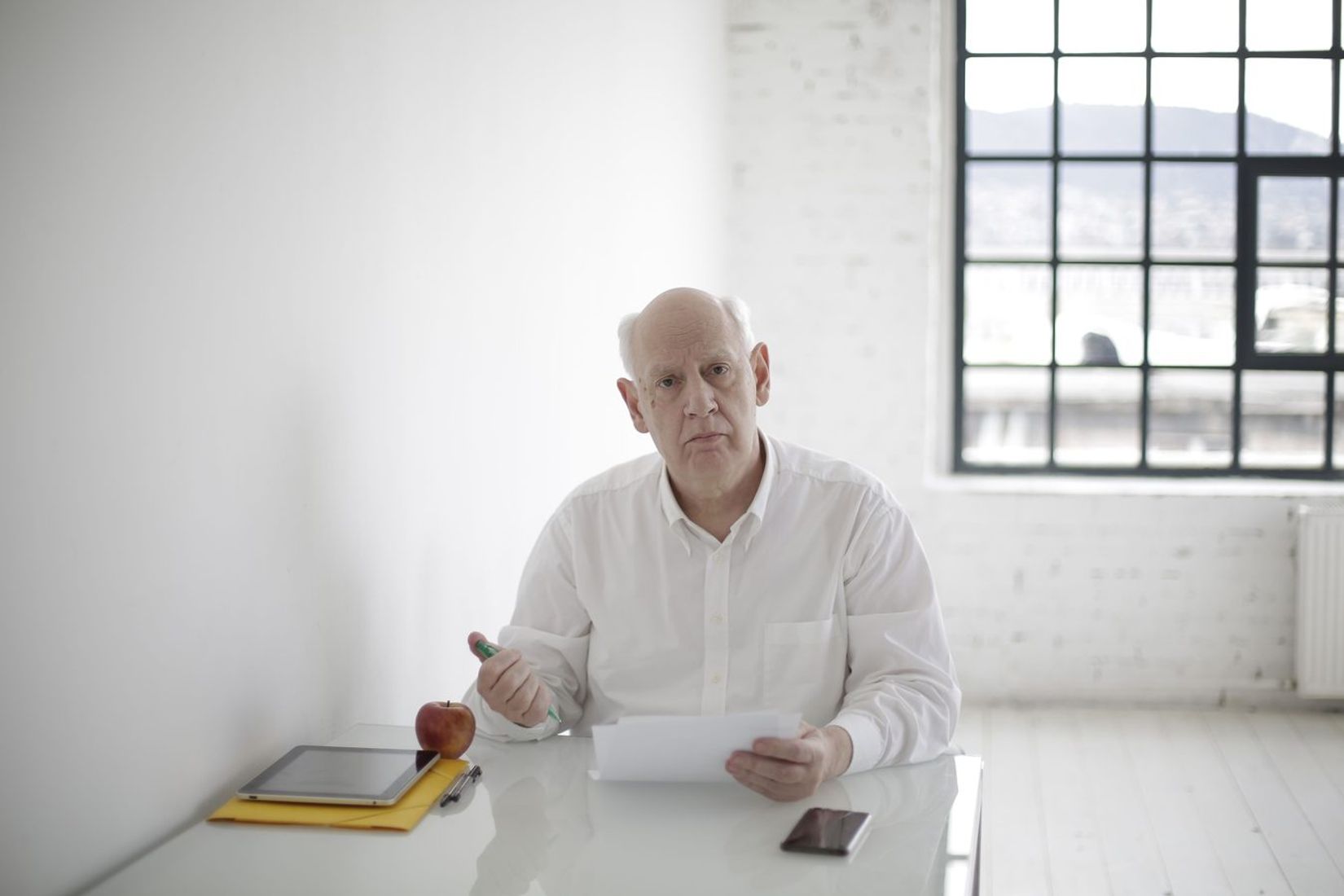 Senior male executive in formal wear sitting at table and signing papers during working day in modern workspace at daytime