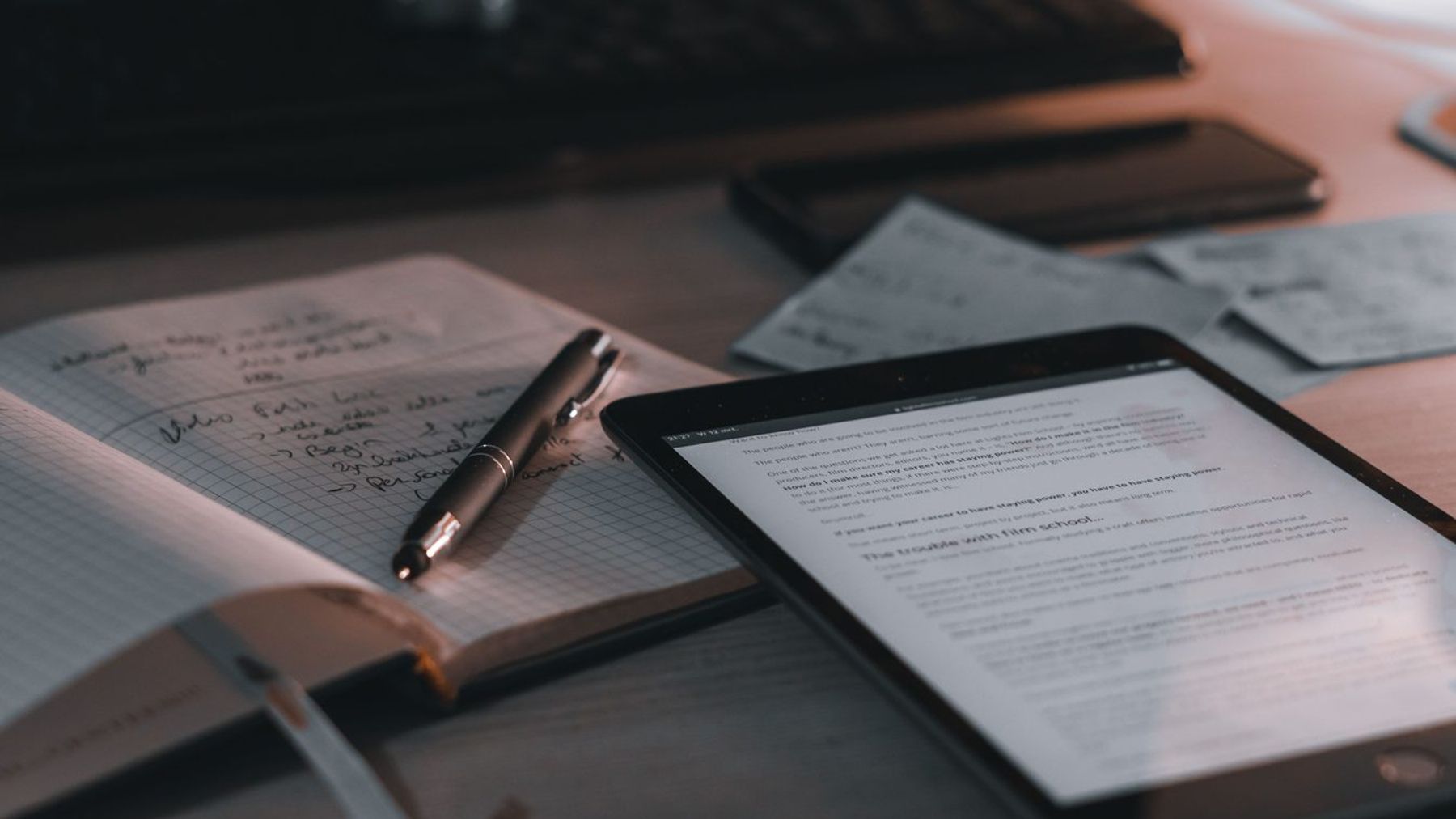 A warm-toned desk setup featuring a tablet, notebook, and pen.