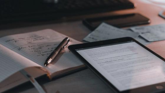 A warm-toned desk setup featuring a tablet, notebook, and pen.
