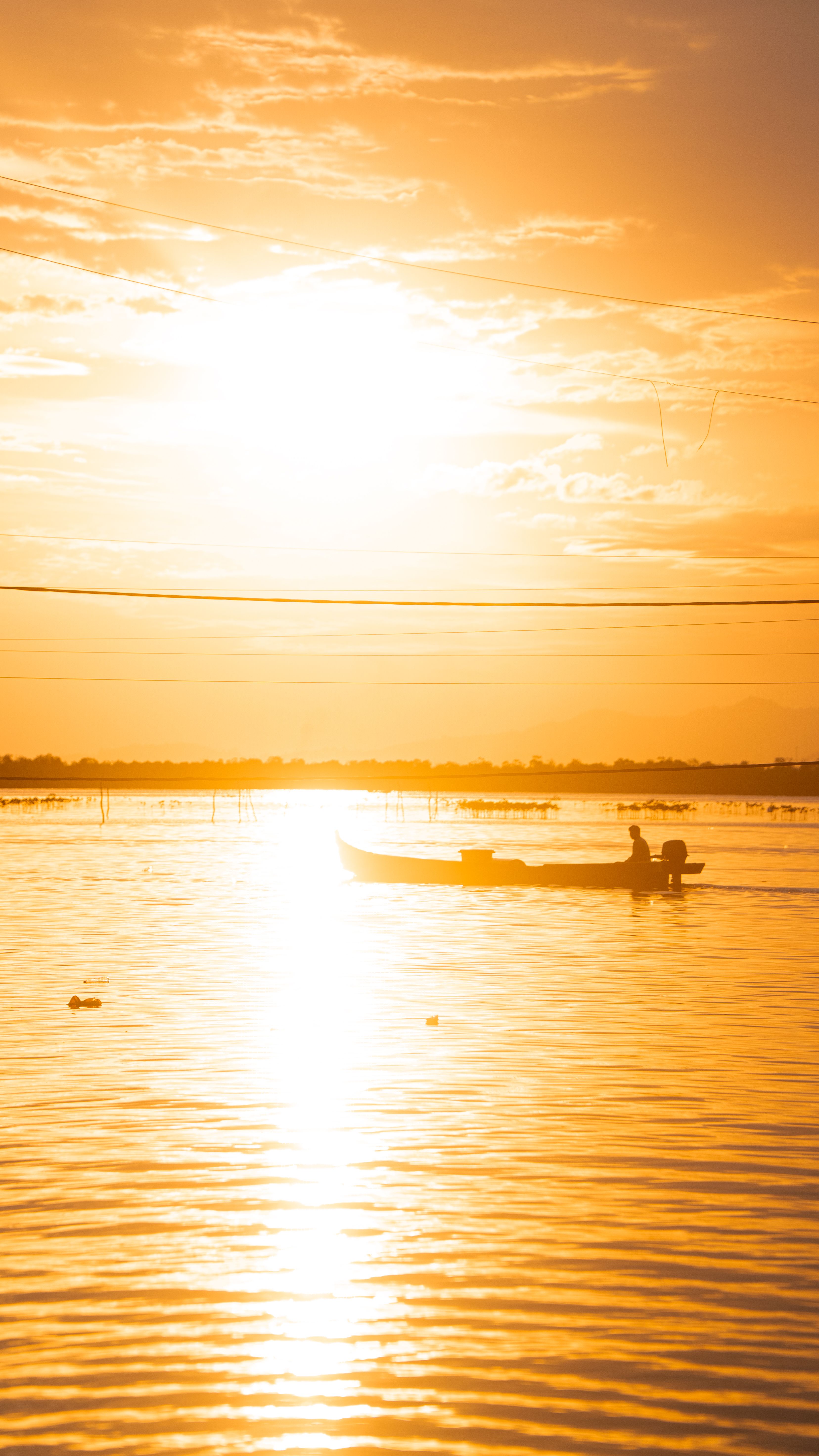 A lone fishing boat silhouetted against the bright golden sunset reflection over Torosiaje waters