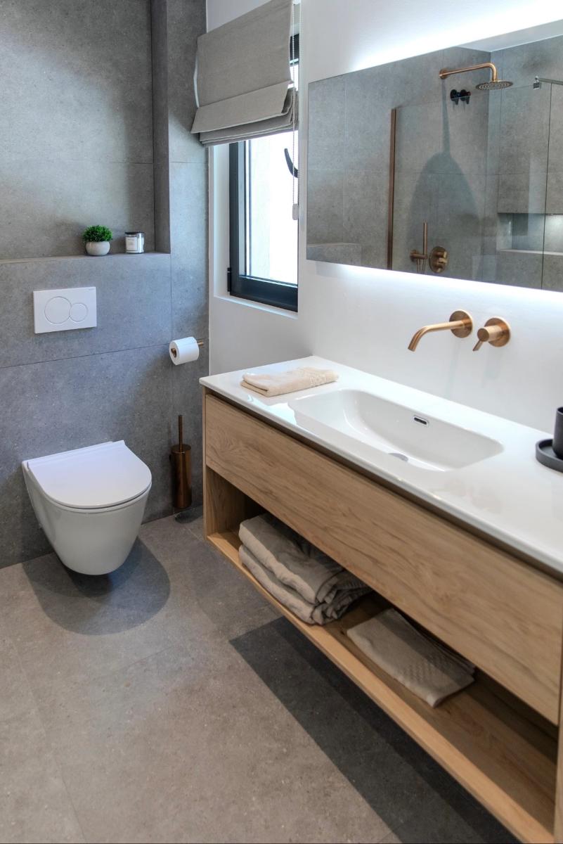 Bathroom in grey stone with oak vanity and brushed bronze fittings