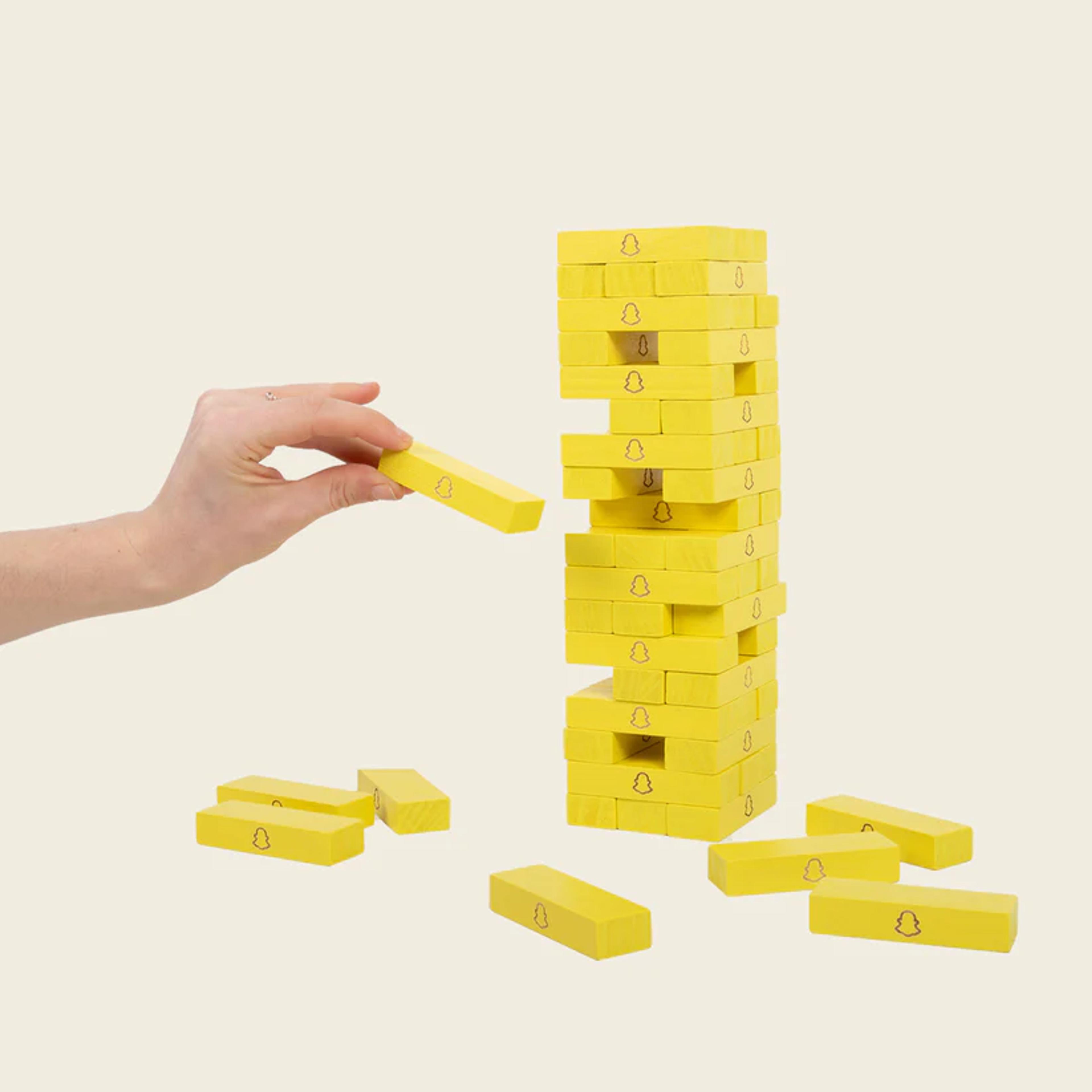 A yellow toppling tower with a hand playing the game