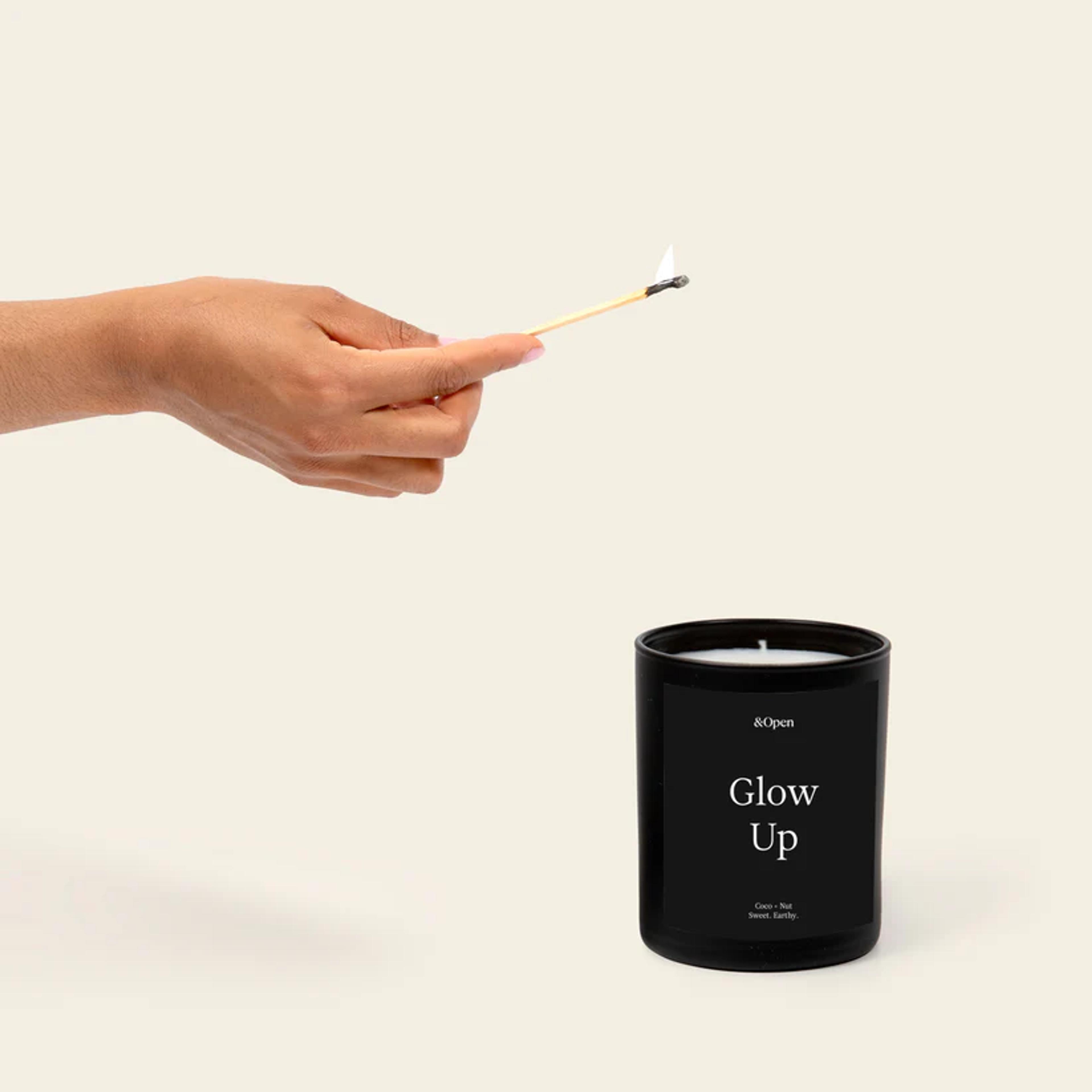 Candle in black glass container with a hand holding a match to light it