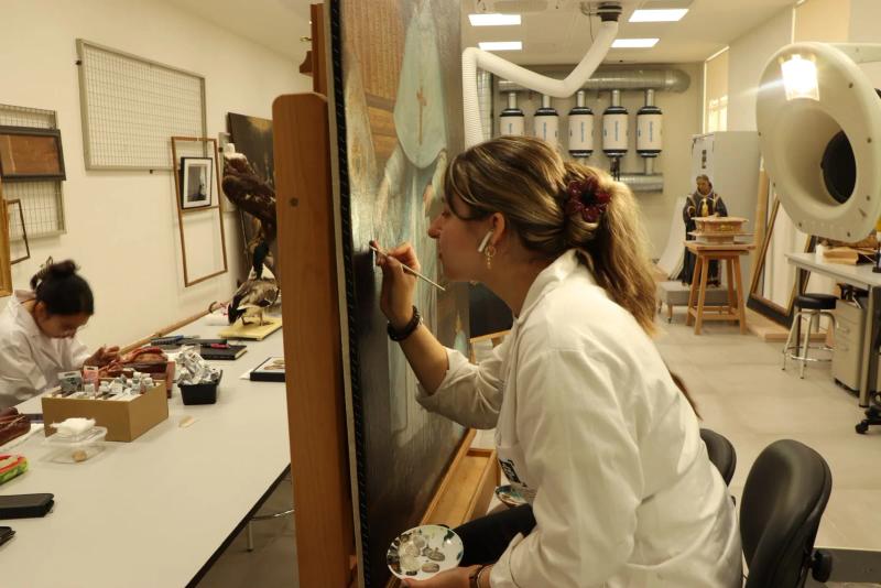 Andrea Casal reintegrando con pincel fino un lienzo sobre caballete en el laboratorio de la Universidad de Granada