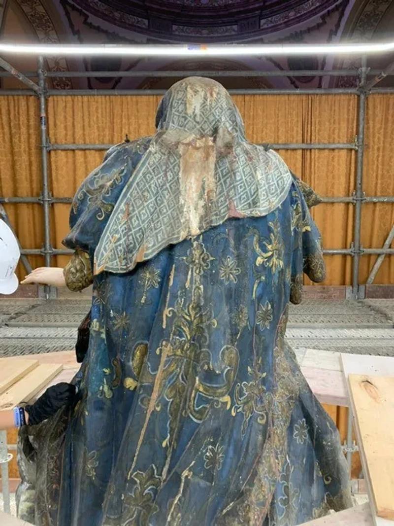 Andrea restaurando sobre el andamio la talla de manto azul y dorado del retablo