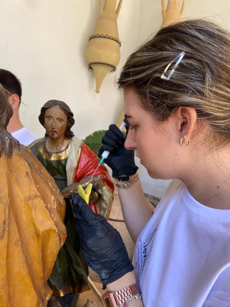 Andrea fijando la policromía de uno de los apóstoles del retablo