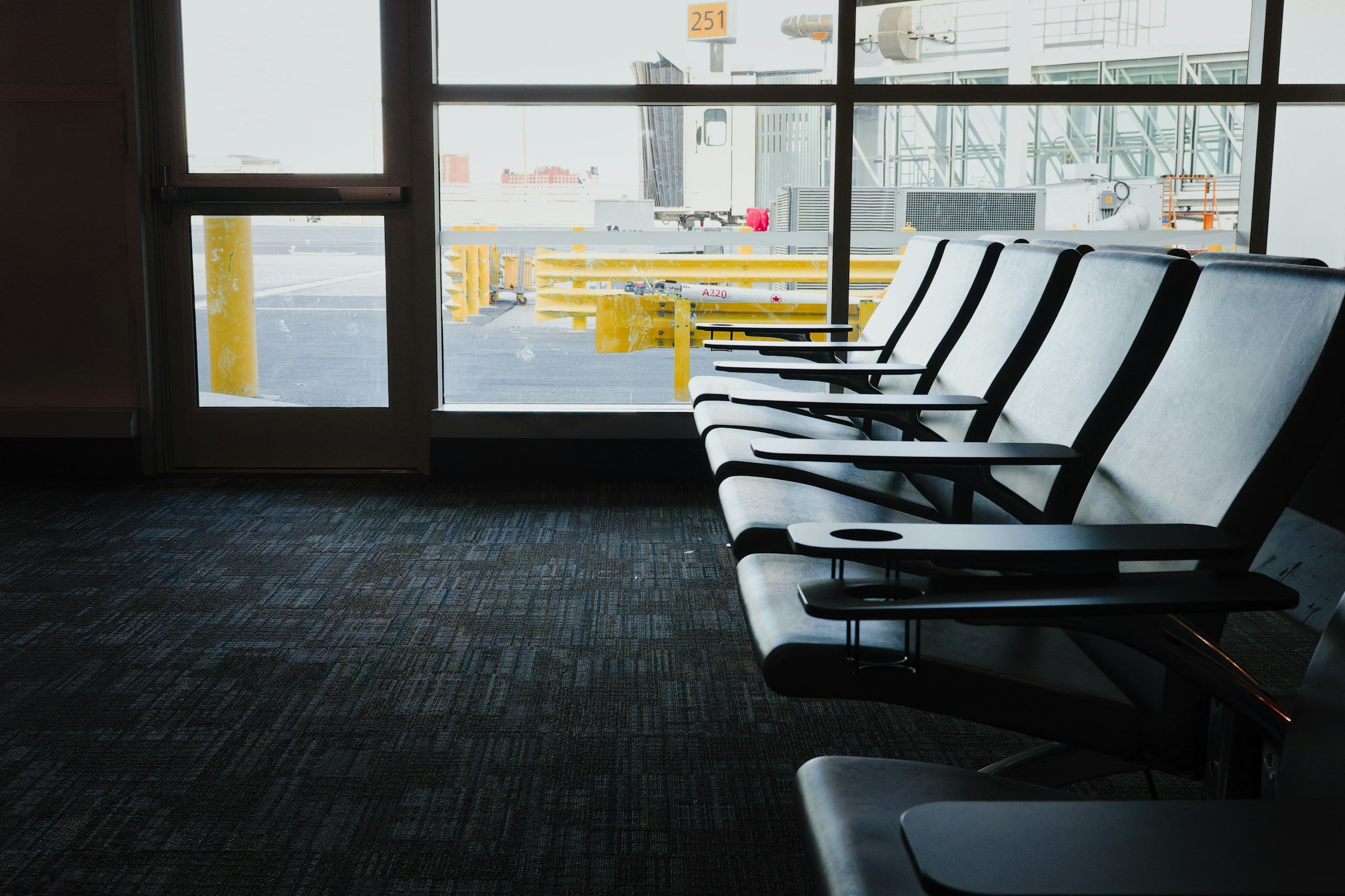 An empty row of airport waiting-area seats facing a window overlooking the tarmac