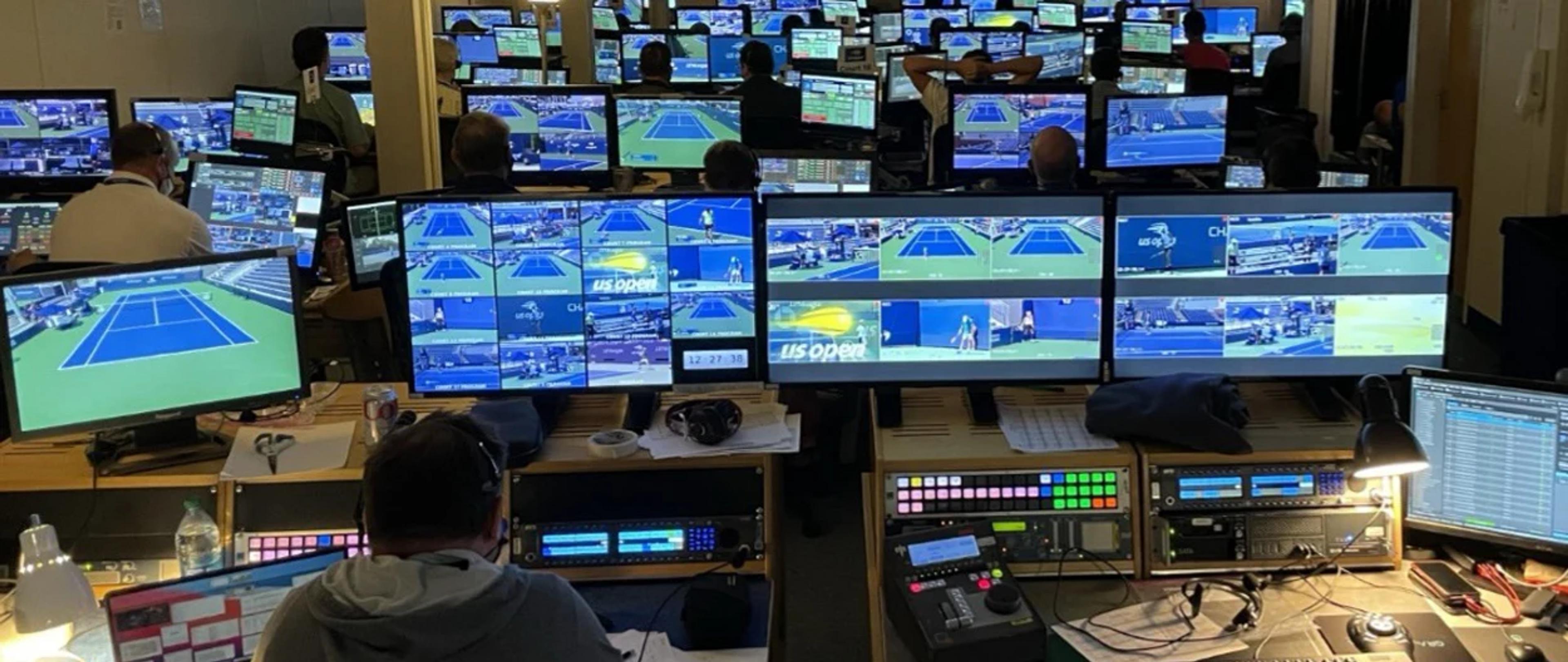 A busy broadcast control room filled with monitors displaying US Open tennis matches, with crew members working at various consoles.