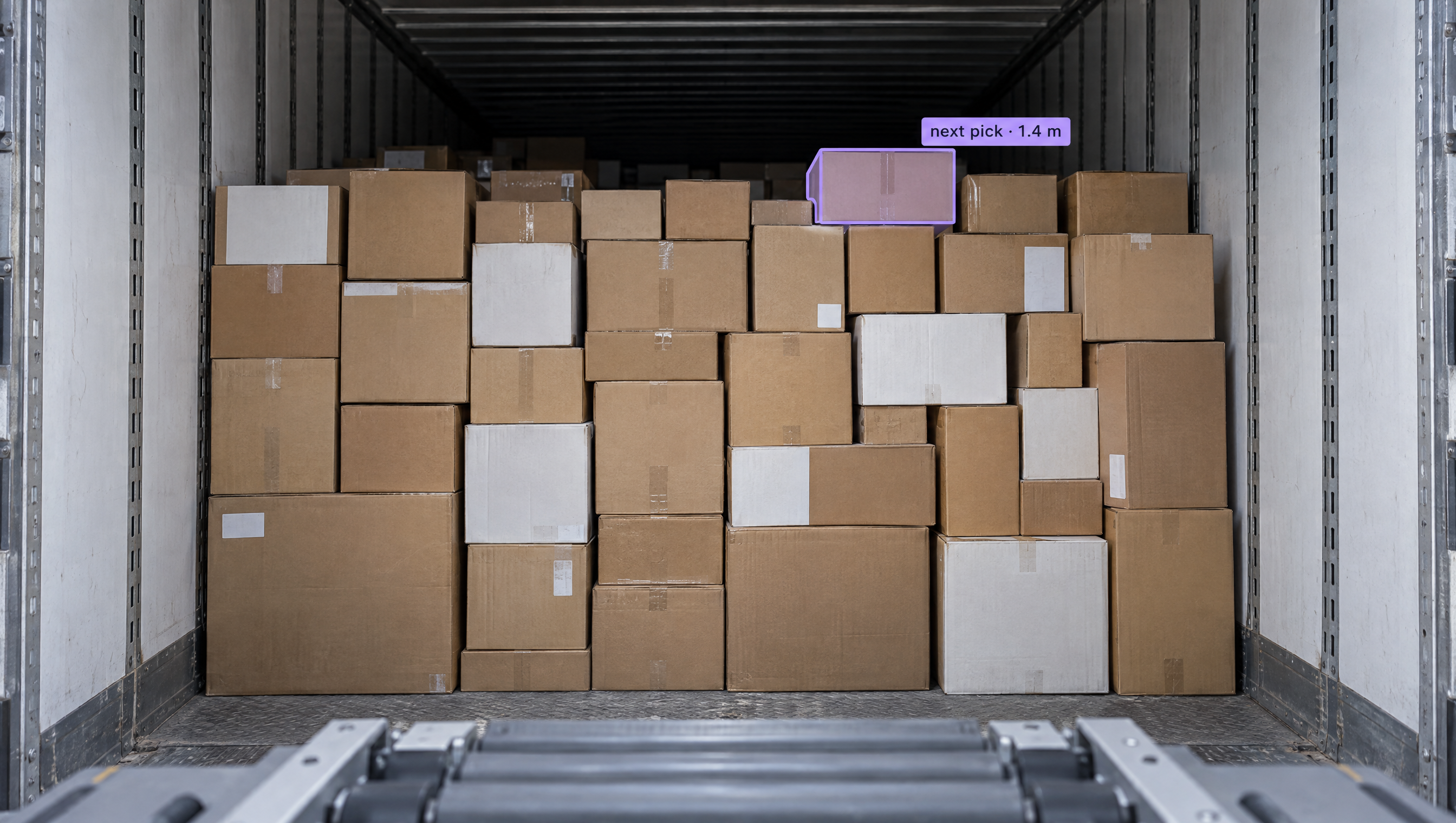 A truck trailer packed with cardboard boxes, one box highlighted with "next pick - 1.4 m", above a conveyor system.