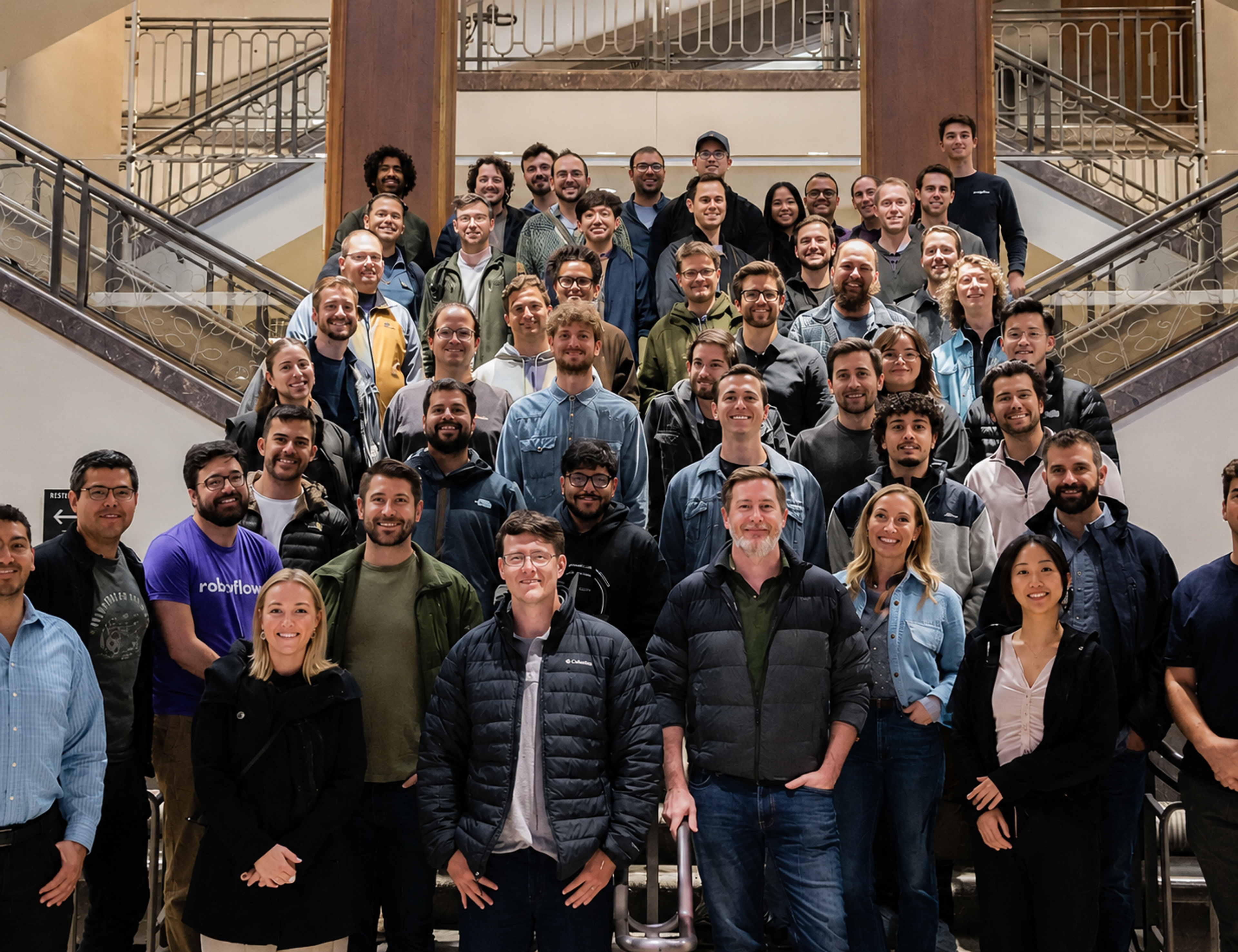 A large group of diverse people poses for a photo on a grand interior staircase.