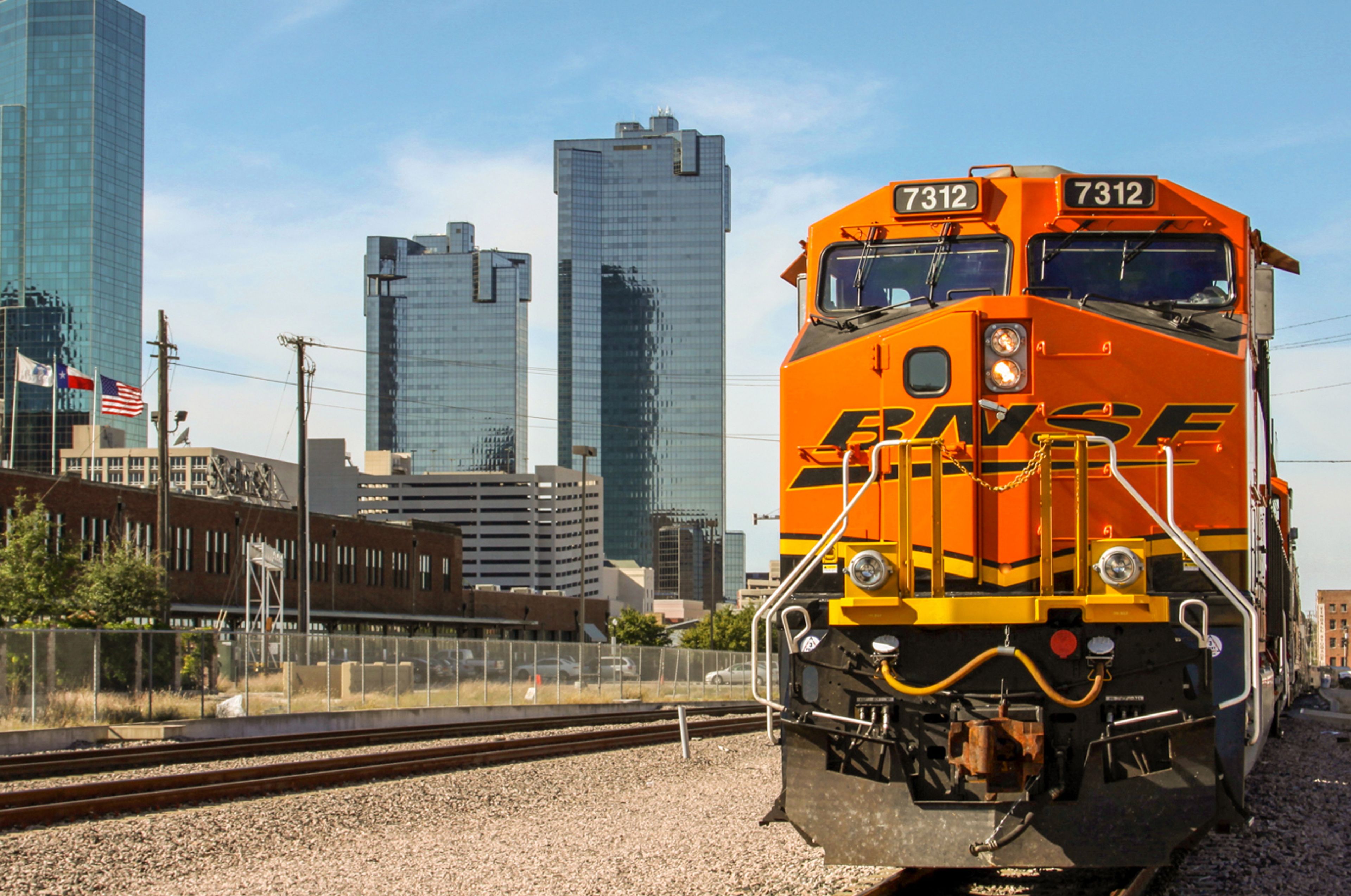 Orange BNSF train 7312 on tracks with a city skyline in the background.