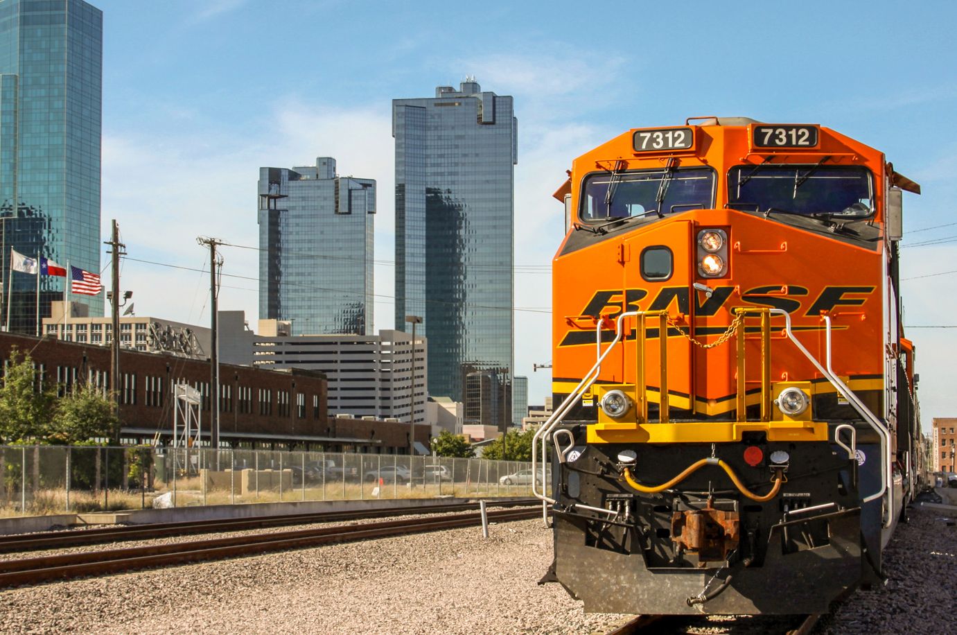 Orange BNSF train 7312 on tracks with a city skyline in the background.