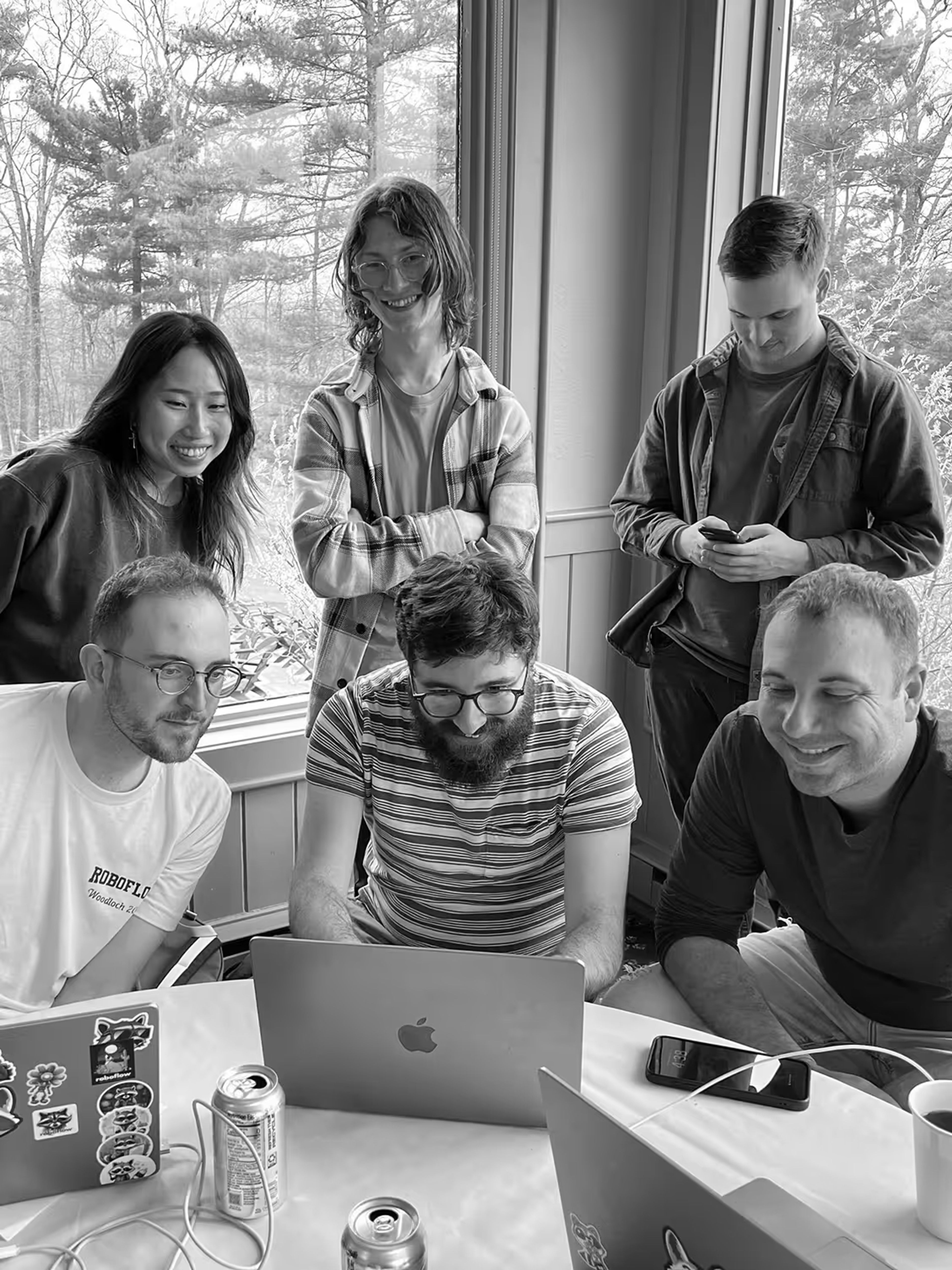 Six people gathered around a table with laptops, smiling and engaged, in black and white.