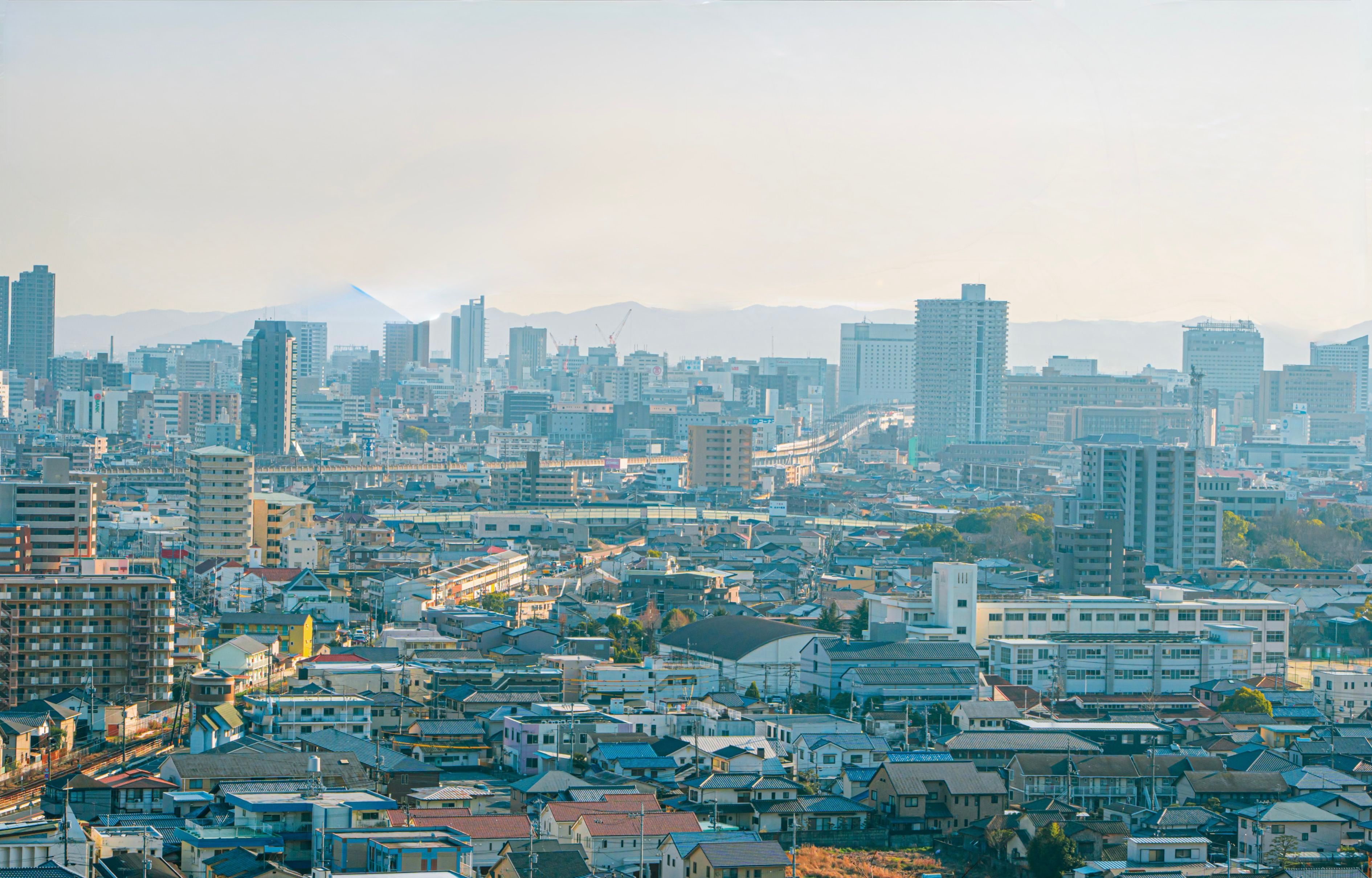 The skyline of Okayama, low rooftops in the foreground giving way to high-rise towers and mountains beyond.