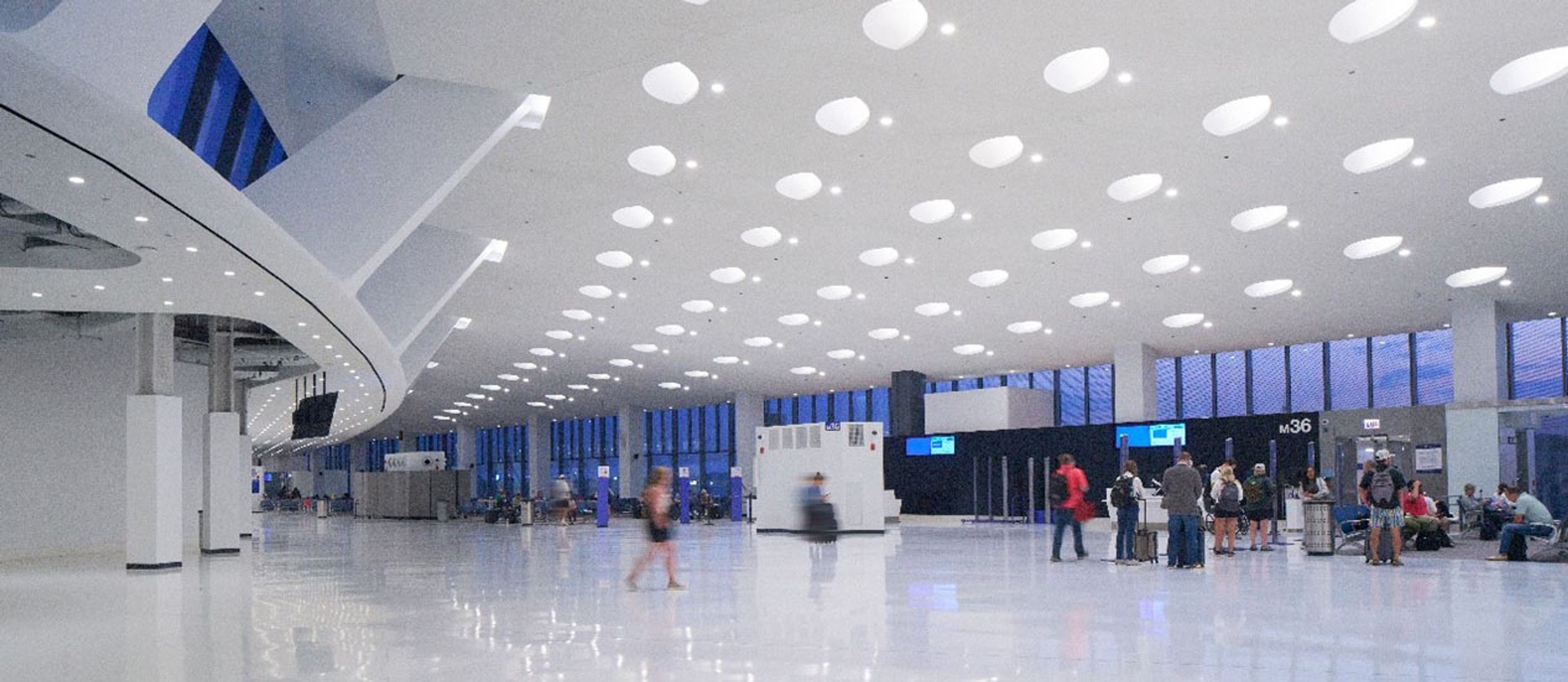 Travelers crossing a bright terminal at Chicago O'Hare beneath a curved white ceiling of USG panels.
