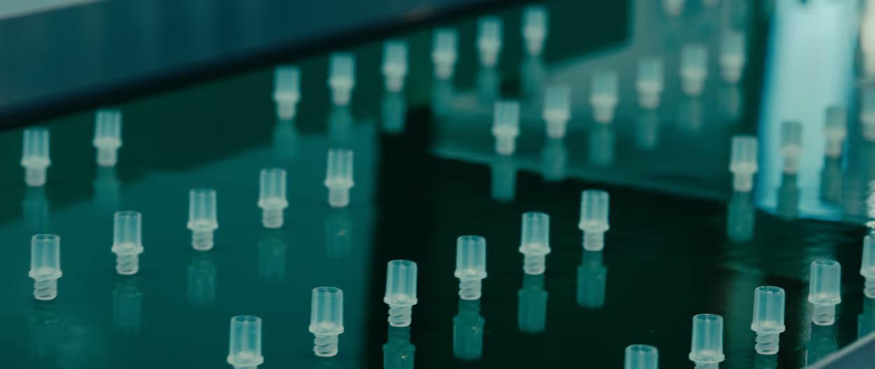 Rows of small, clear, threaded plastic components on an industrial production line.