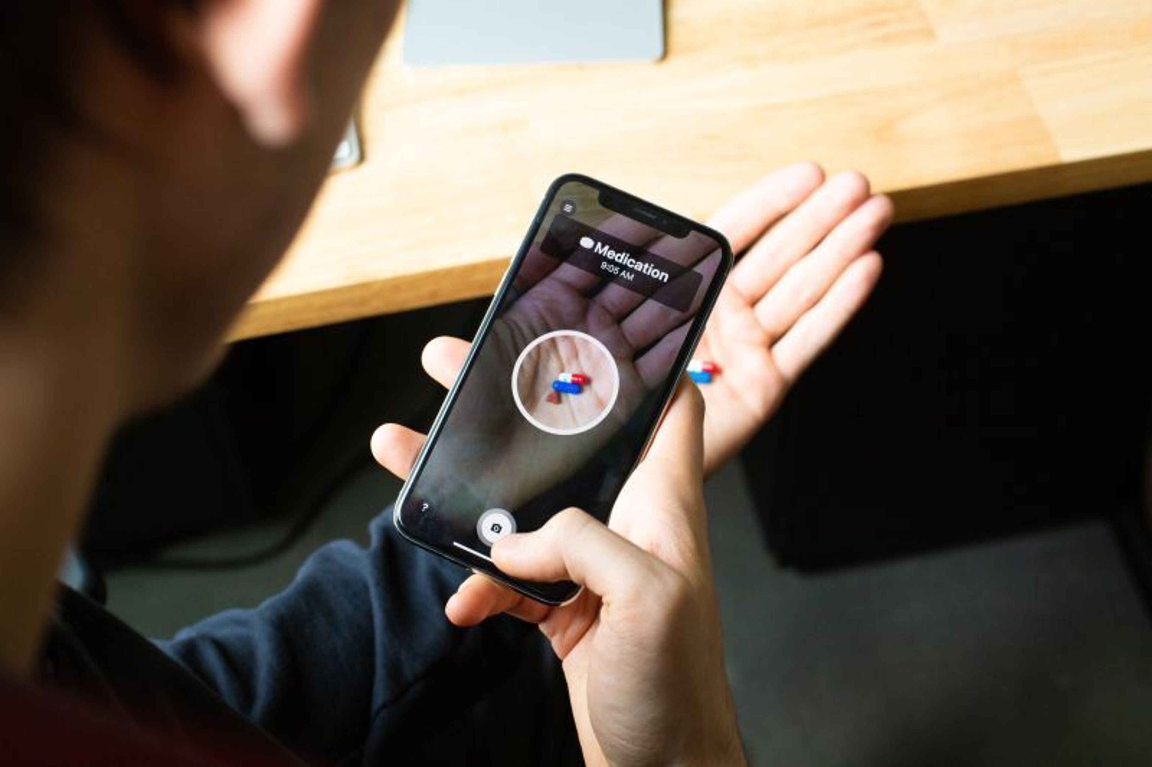 A person holding a phone that photographs two pills in their palm, the Wellth app circling the medication.