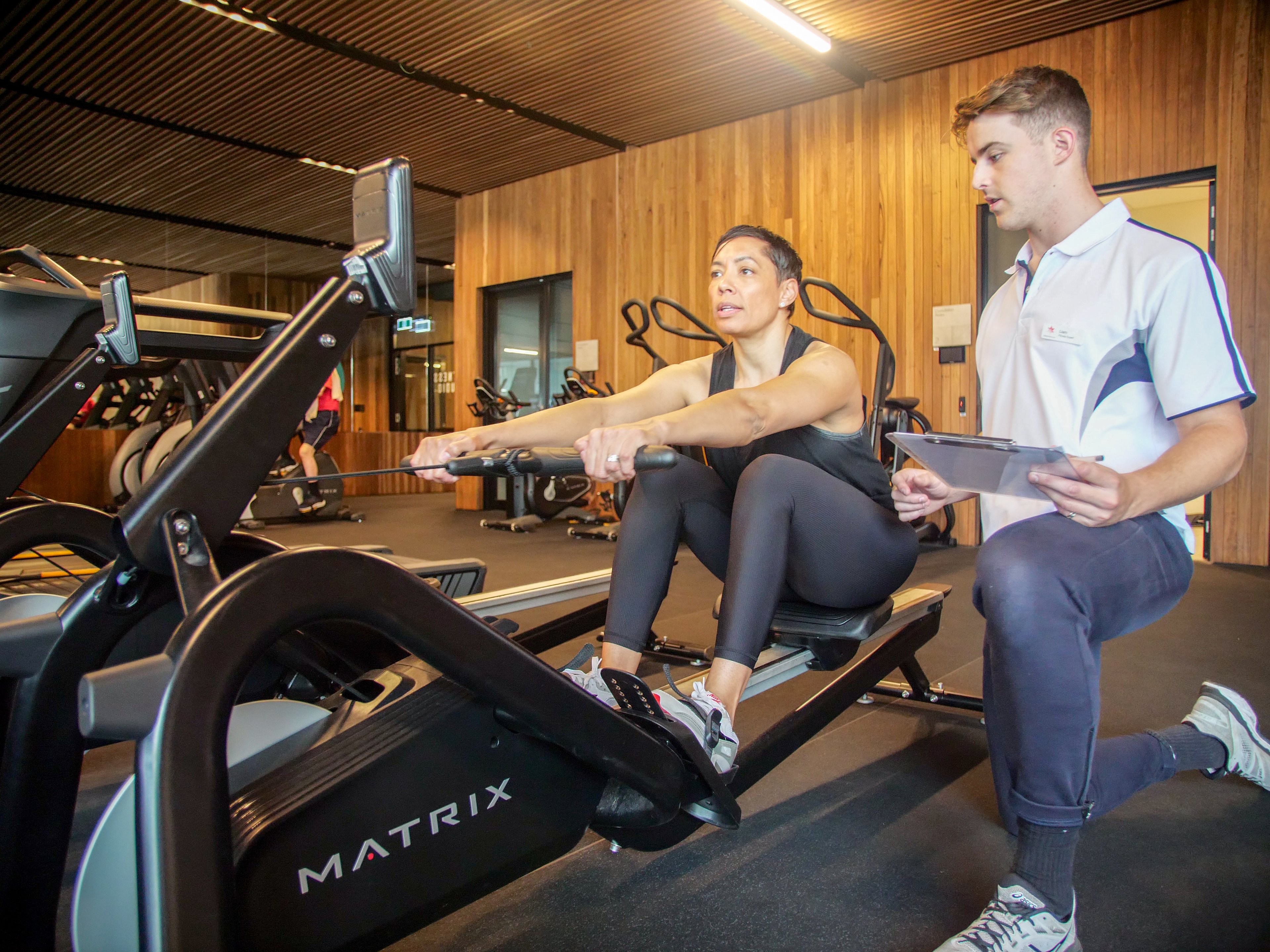 Personal trainer watches participant using the rowing machine