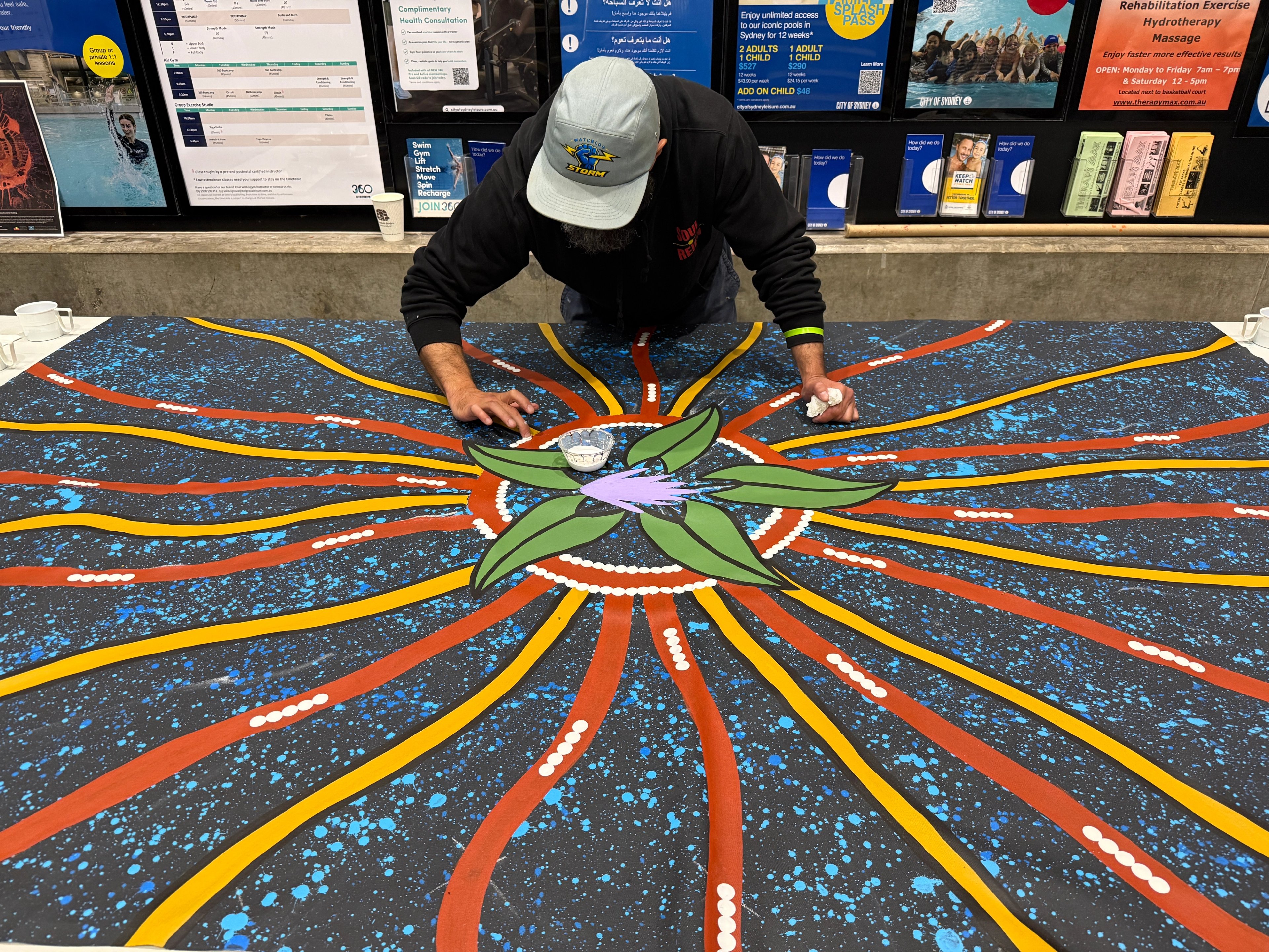 Artist Lyle Ah Sam painting on a large canvas at Cook + Phillip Park Pool