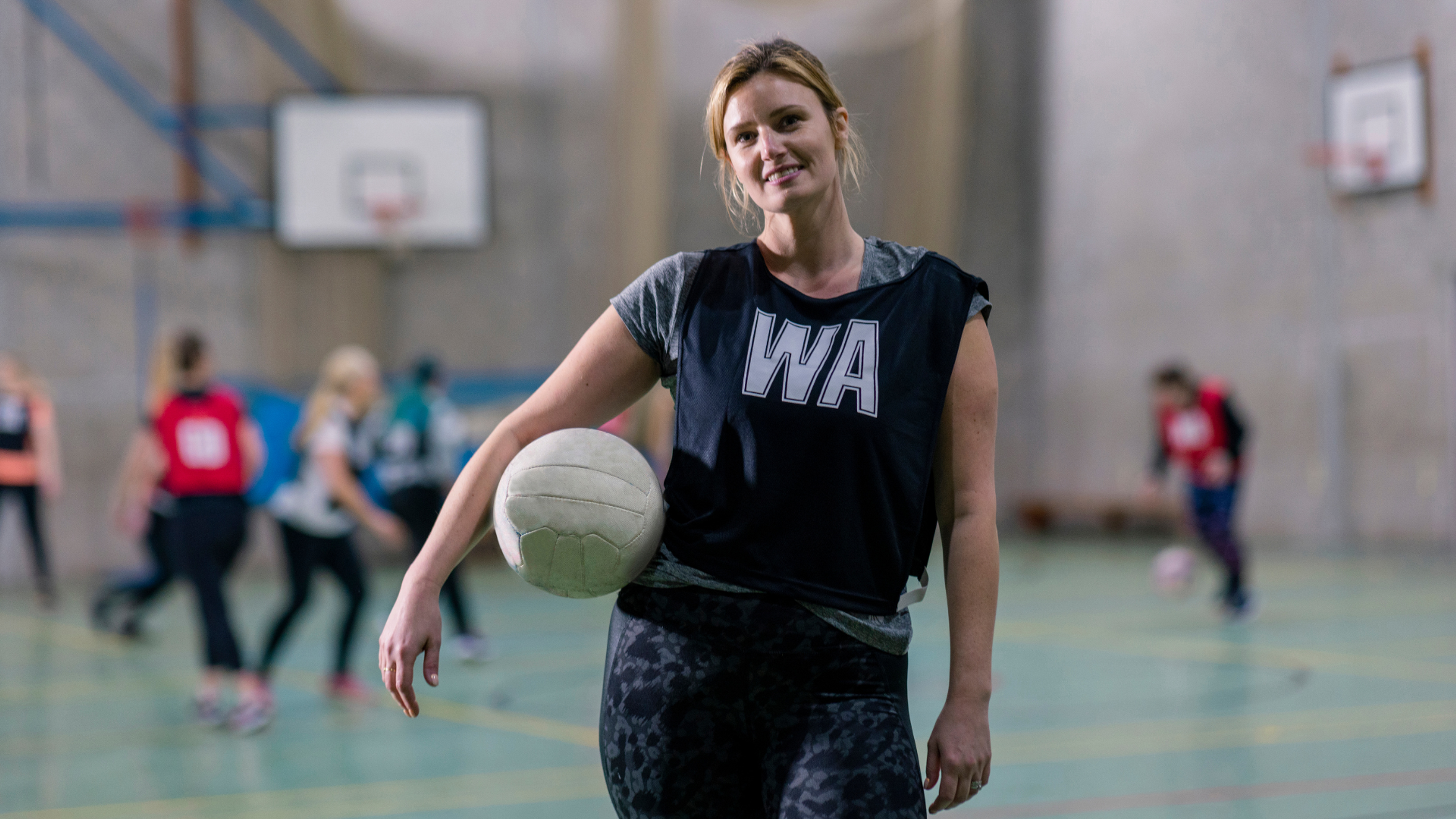 Woman holding a ball and smiling while wearing a netball bib