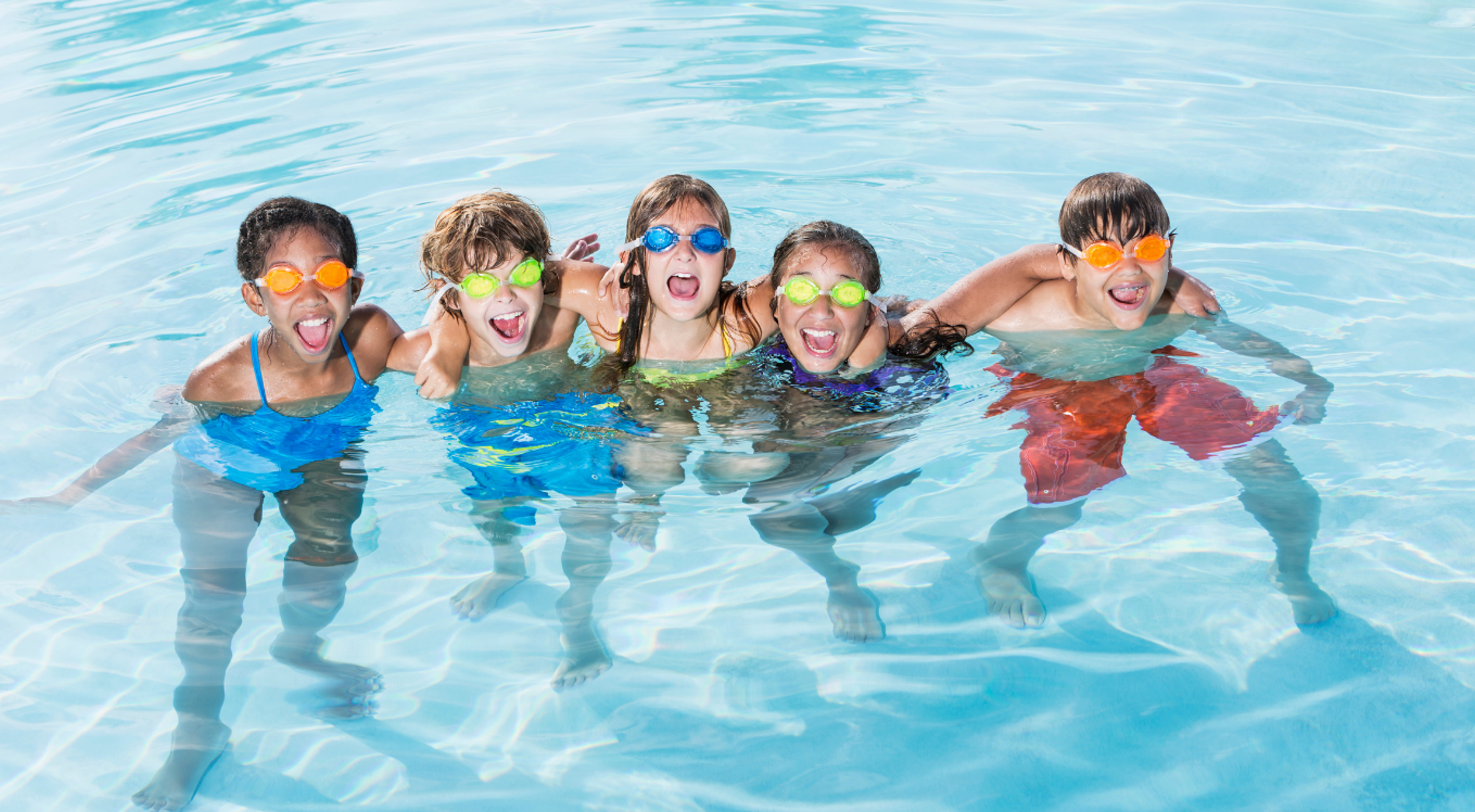Five children standing in a pool and wearing goggles and smiling 