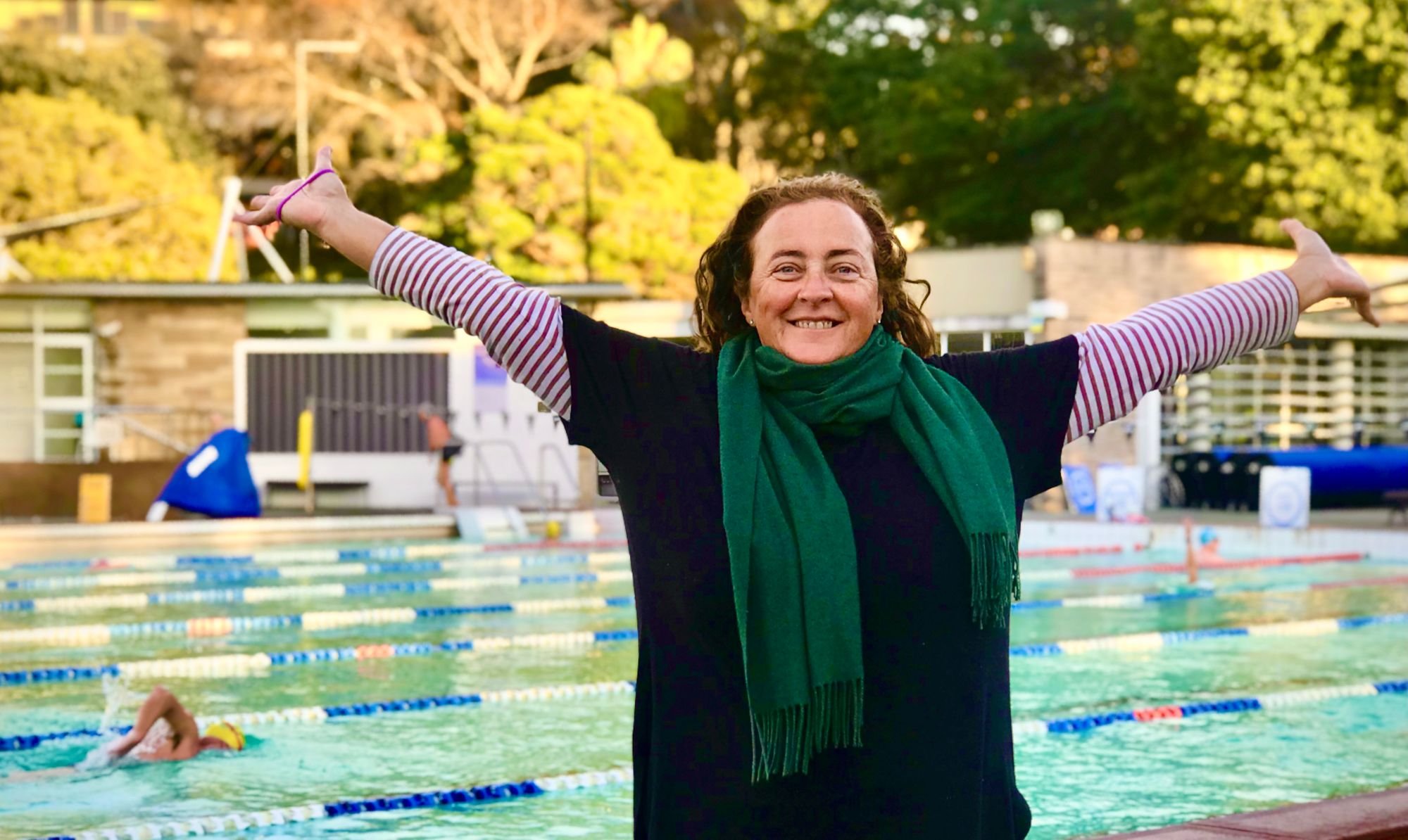Dawn smiling with her arms stretched out in front of Victoria Park Pool