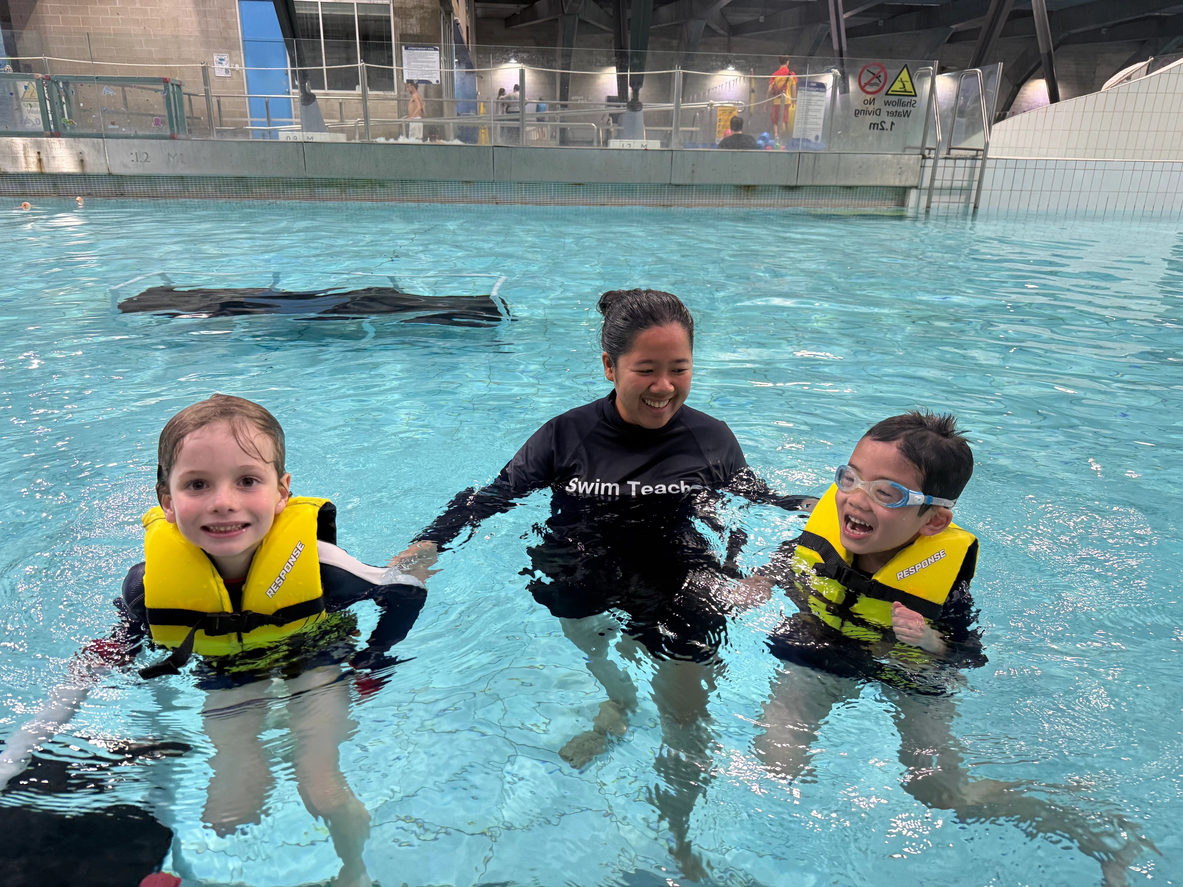 Two young kids wearing life jackets in the pool with a swim teacher at Cook + Phillip Park Pool