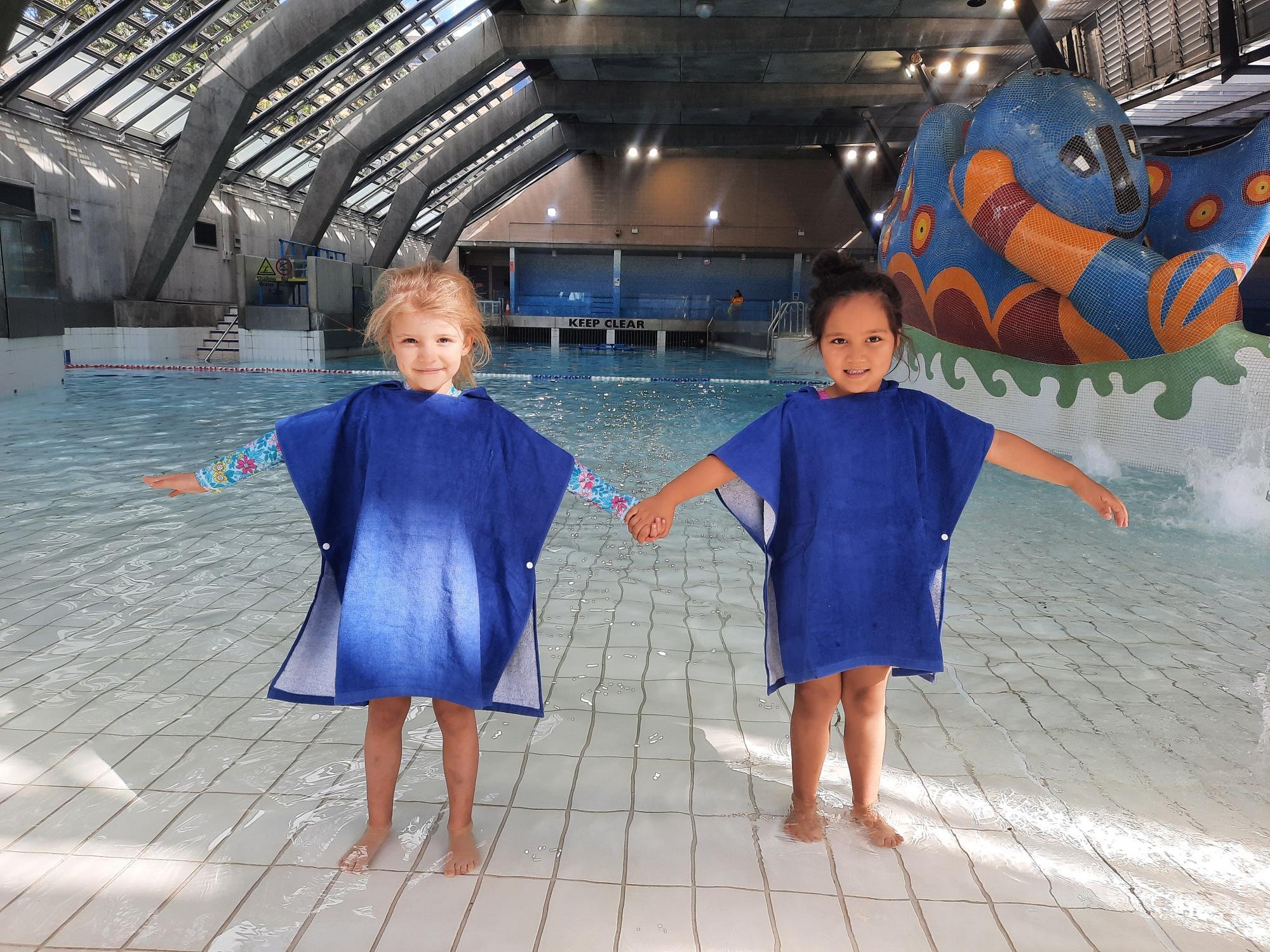 Two girls smiling and holding hands in front of the Cook + Phillip Park Pool