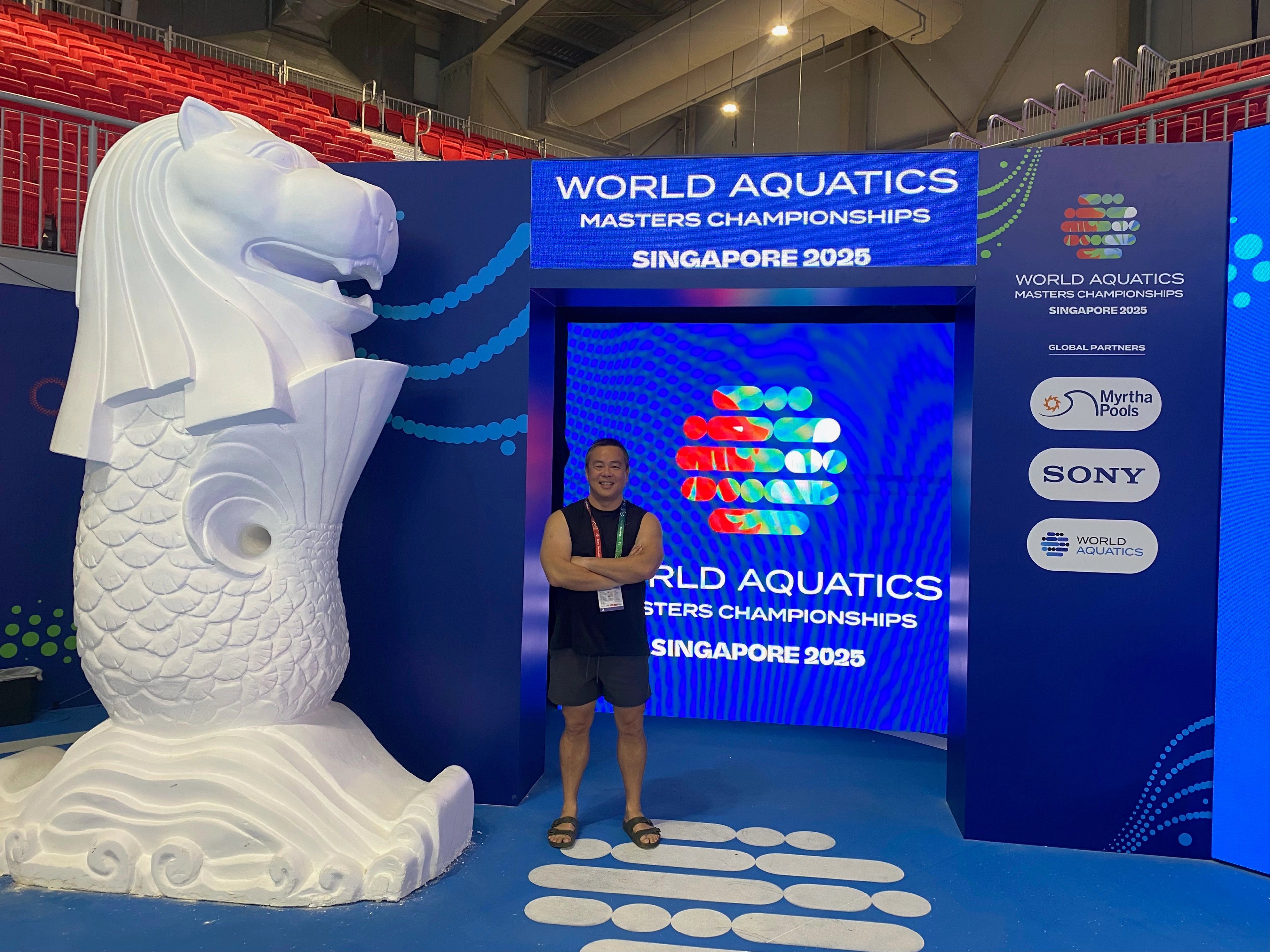 Edmund standing with his arms crossed, in front of a blue and white screen that displays the World Aquatics logo
