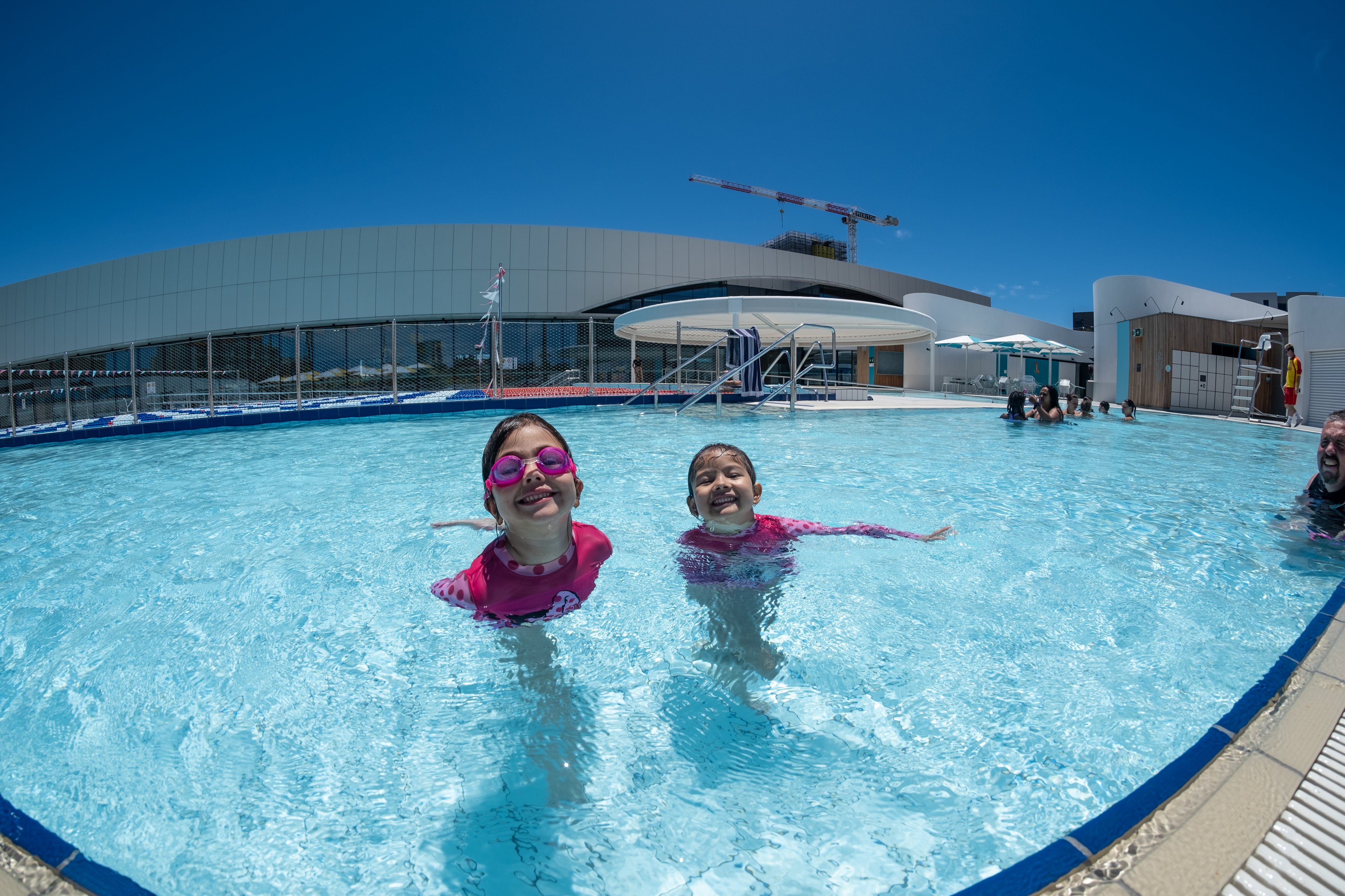 Two kids smile while swimming outdoors in the 50m pool at Gunyama Park
