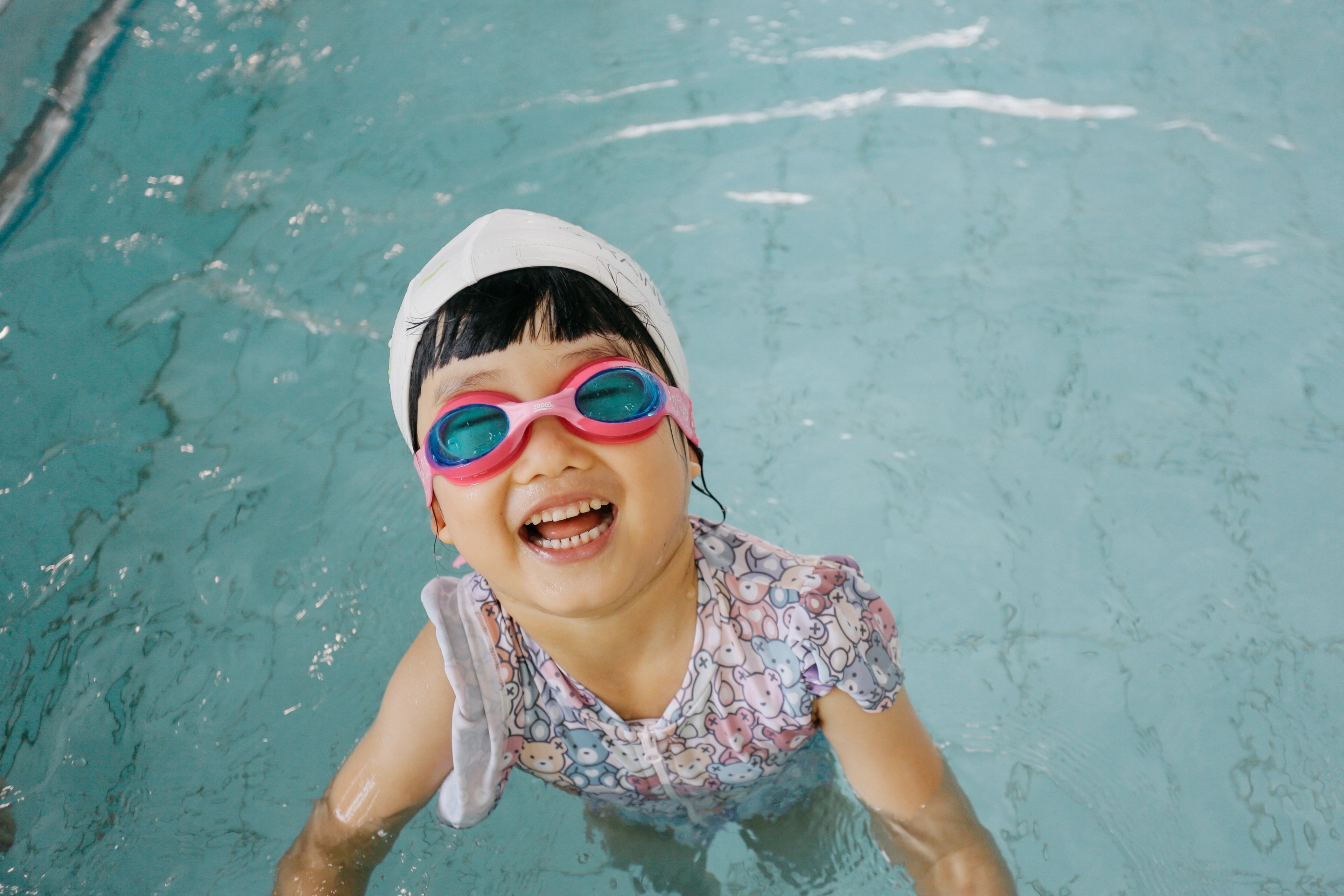 Young girl wearing goggles in the pool and smiling at the camera 