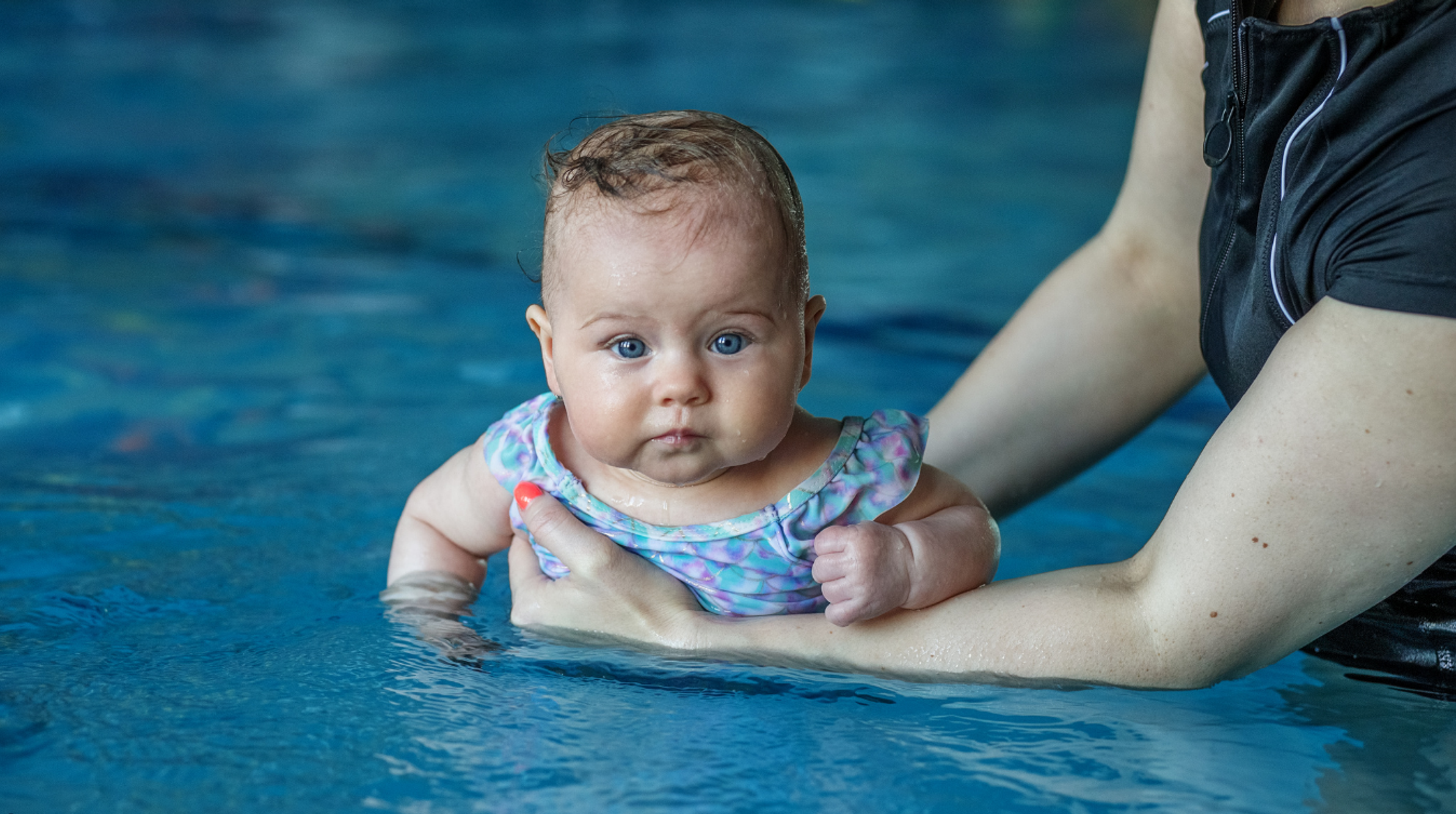 Baby being held by an adult while in the pool 