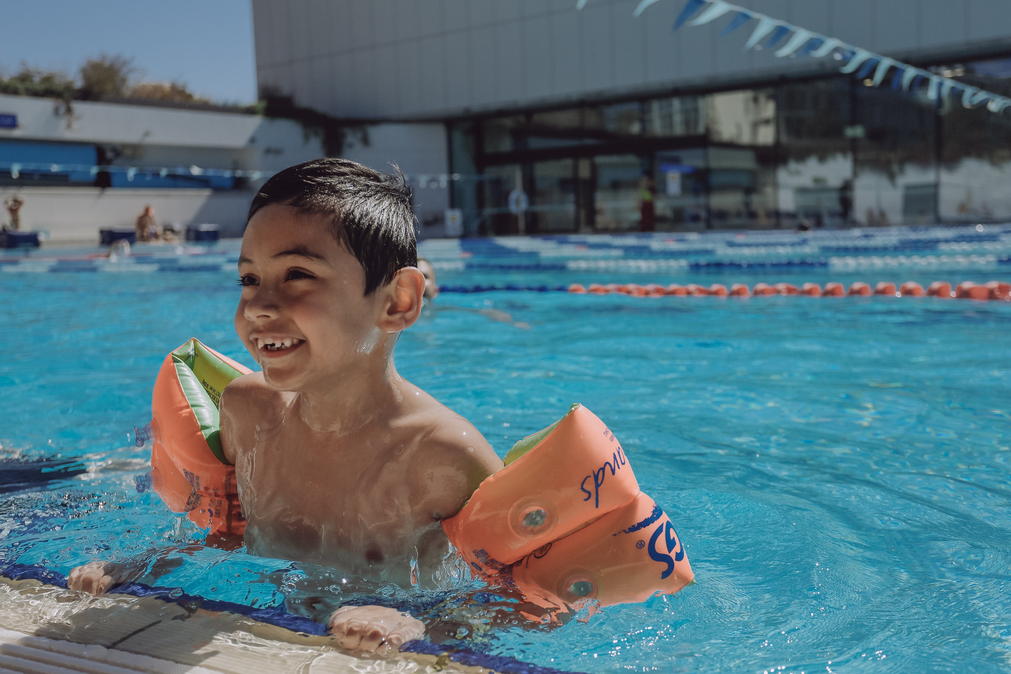 Three young kids in the pool floating on pool noodles and looking at the camera and smiling