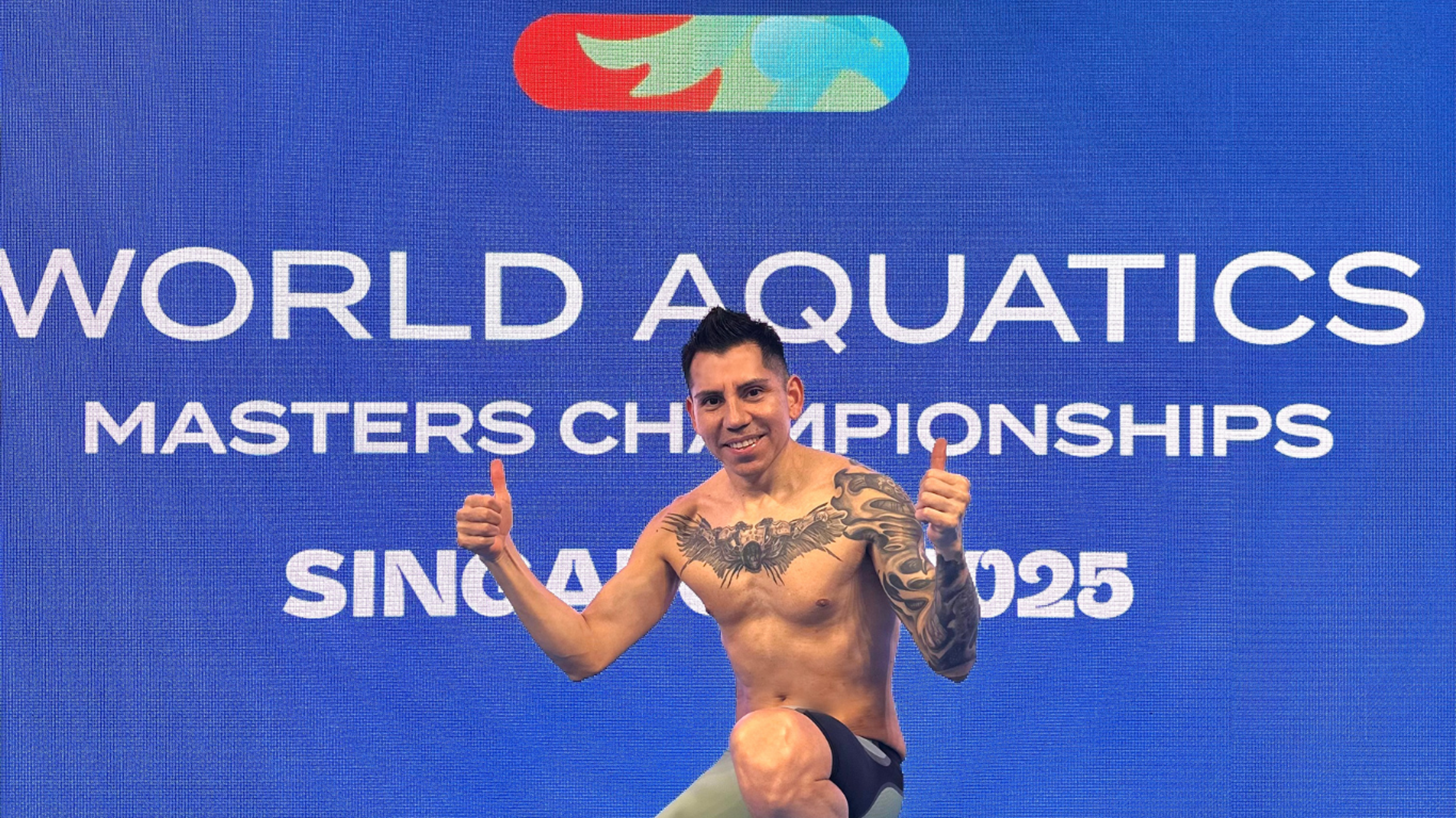 Socrates posing with his thumbs up in front of the World Aquatics screen 