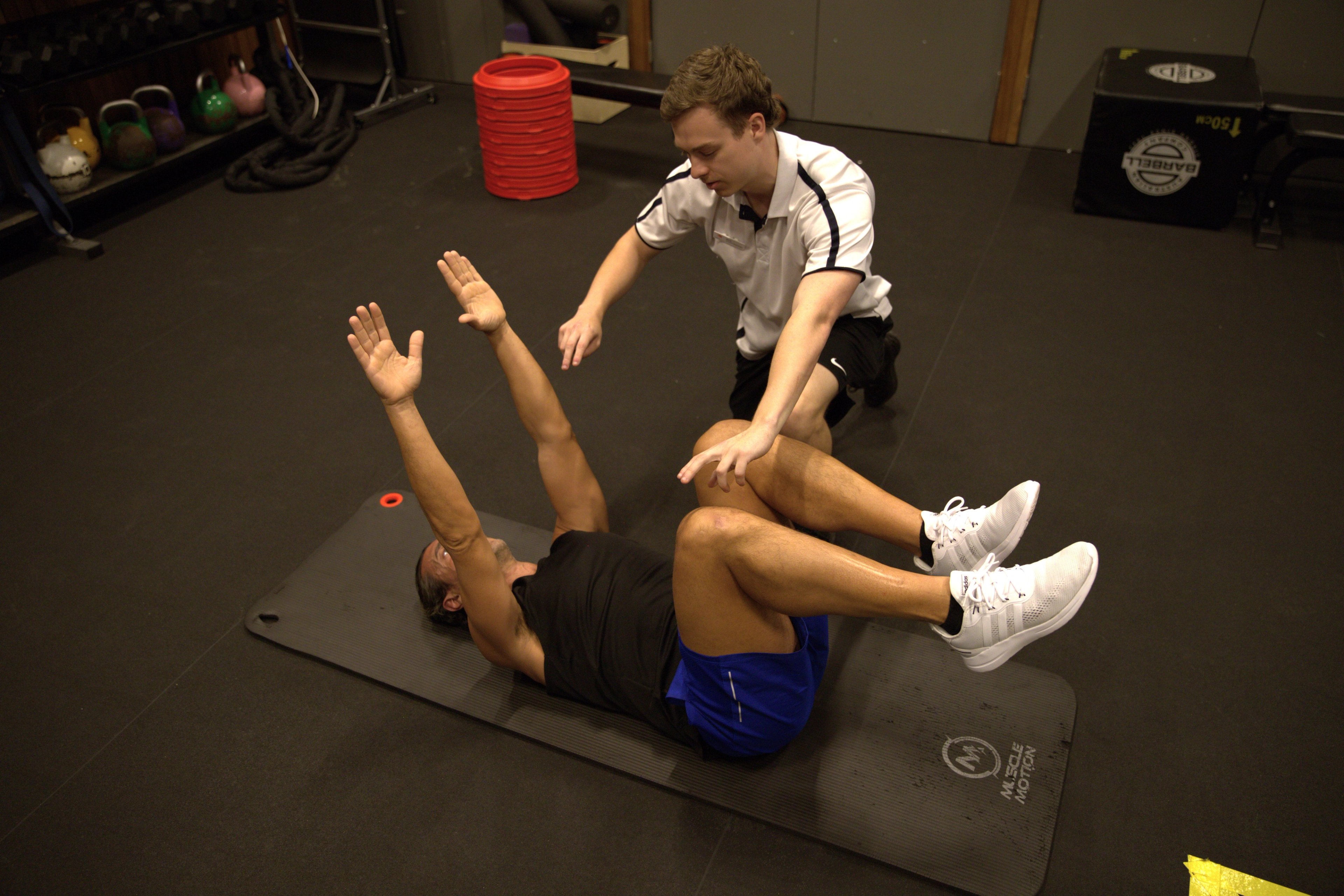 Exercise Physiologist Nick assisting a client with floor stretches during an EP session at Gunyama Park 