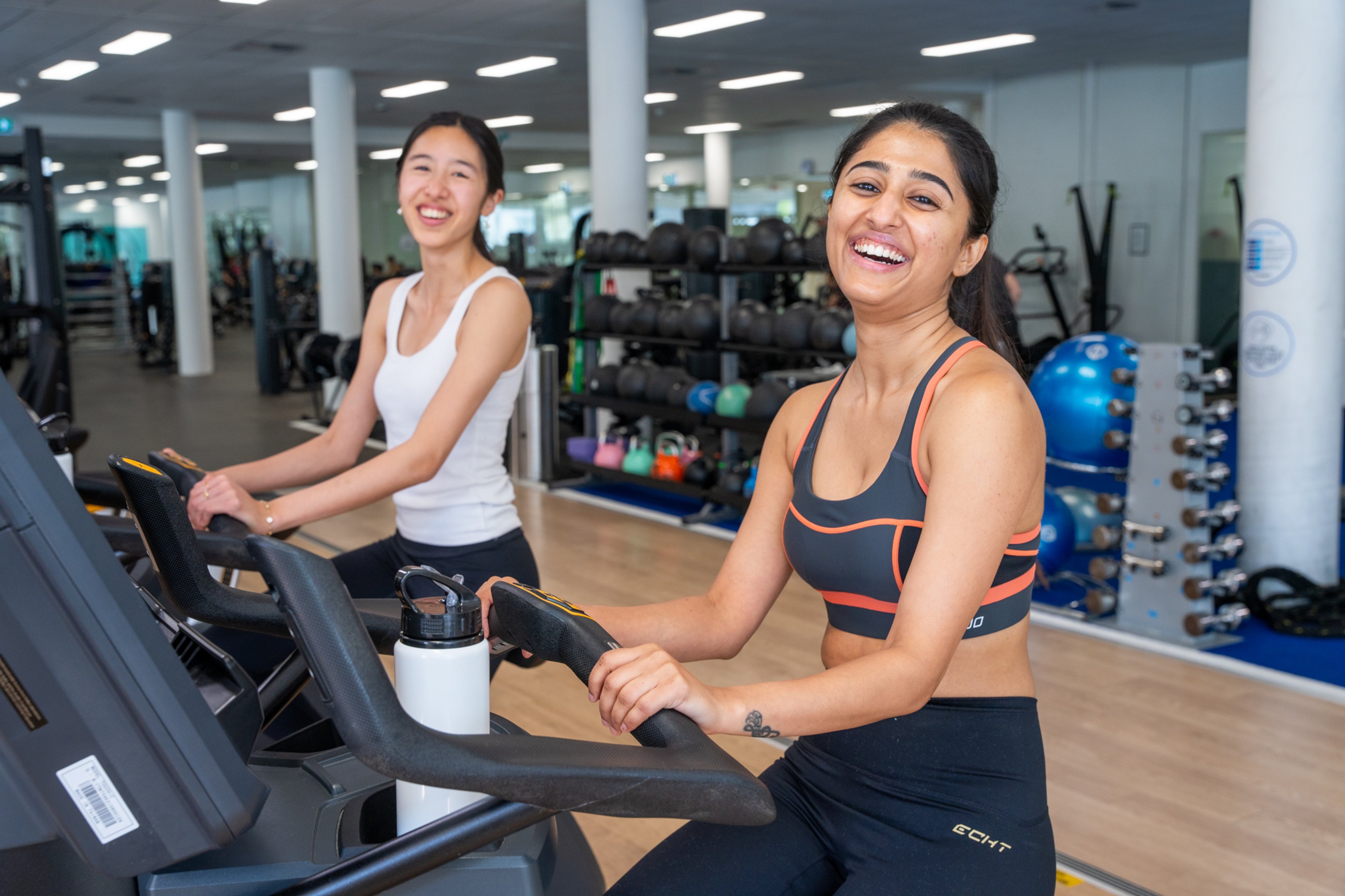 Two women smiling while on exercise bikes at Ian Thorpe Aquatic Centre gym