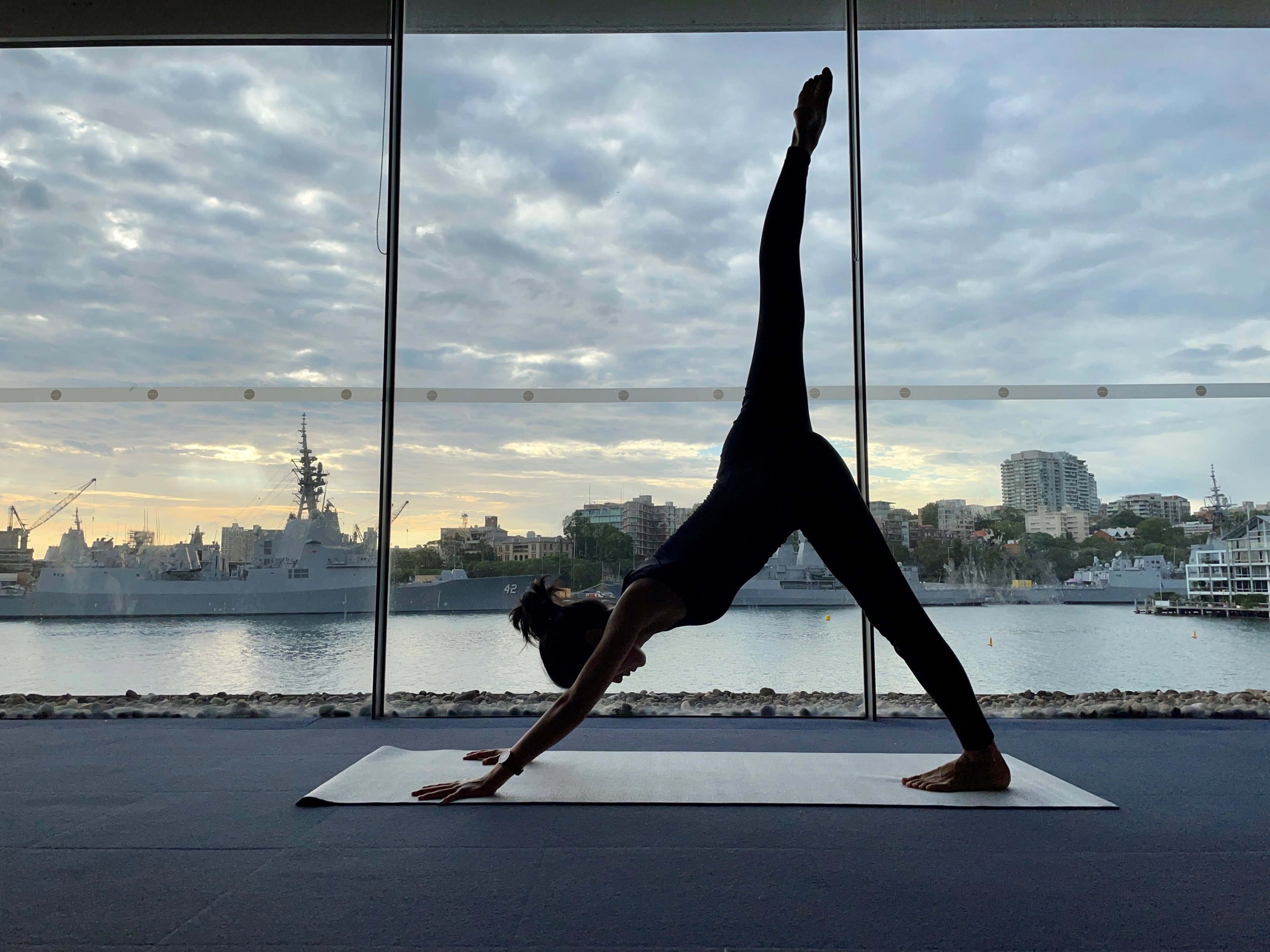 A woman holding a yoga pose in the Andrew (Boy) Charlton fitness studio, with the view of Woolloomooloo Bay in the background