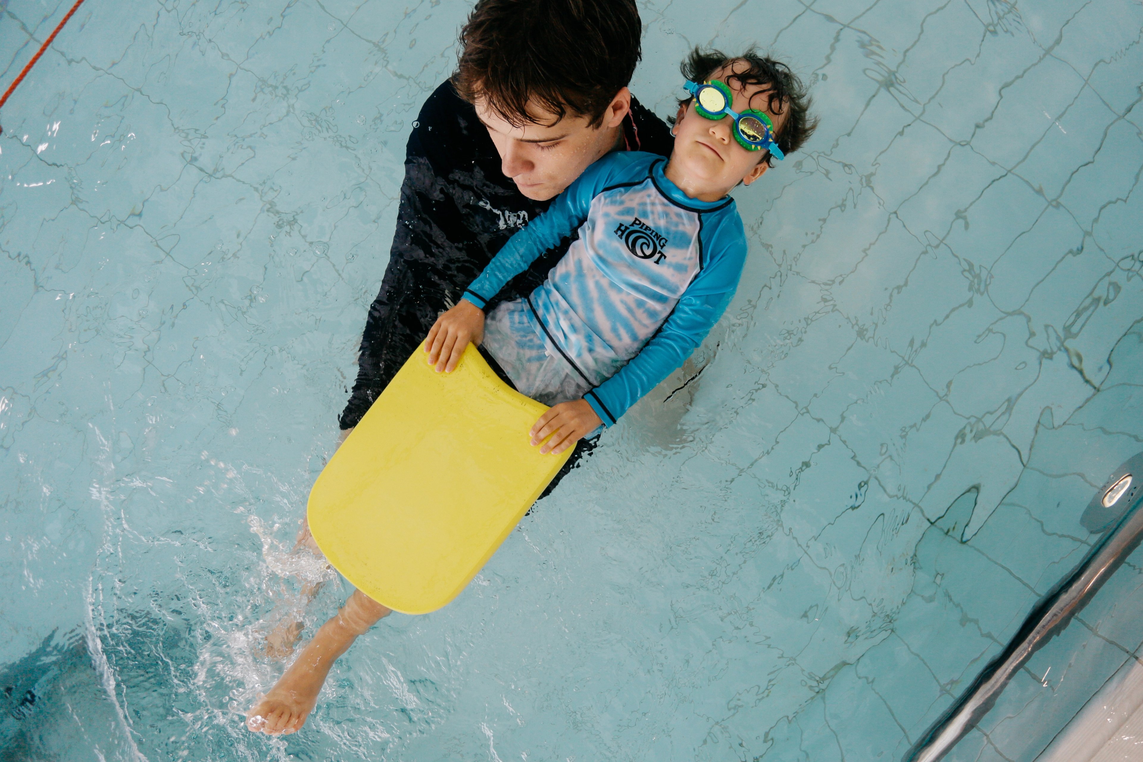 A child laying back in the pool with a kickboard during a swim lesson with the instructor 