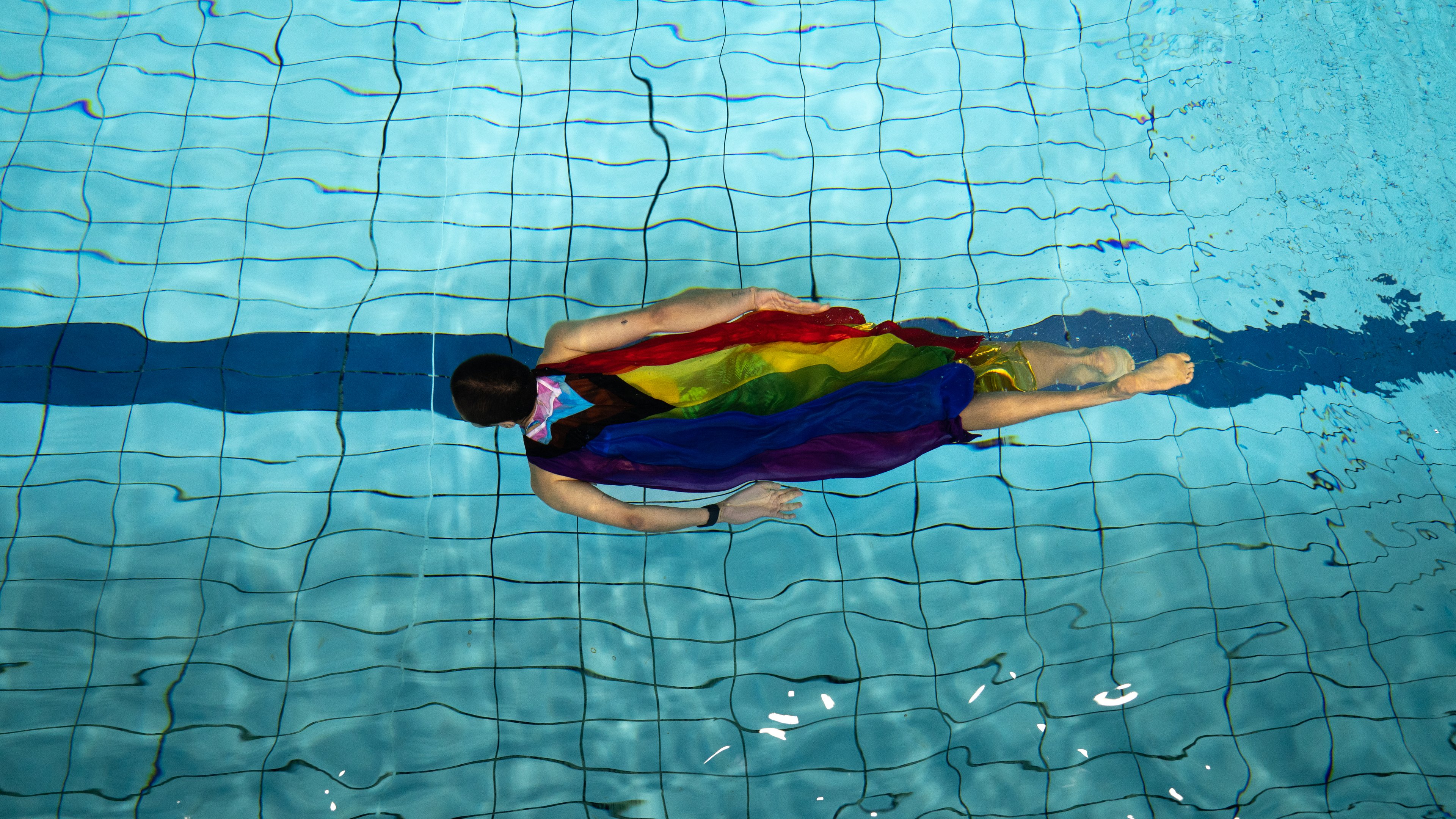 Person swimming underwater with the pride flag