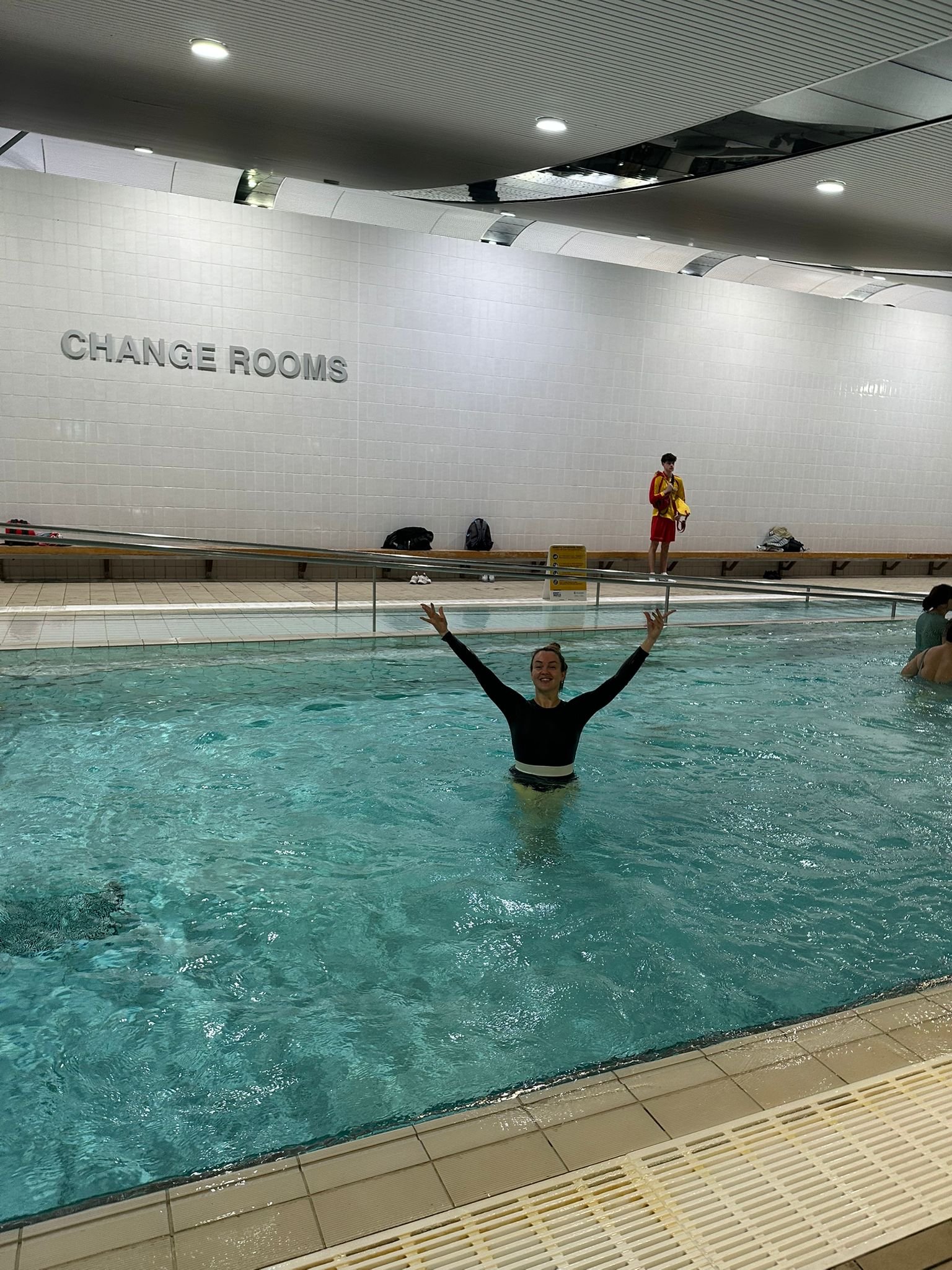 Class participant Morena in the pool with her hands in the air at Ian Thorpe Aquatic Centre