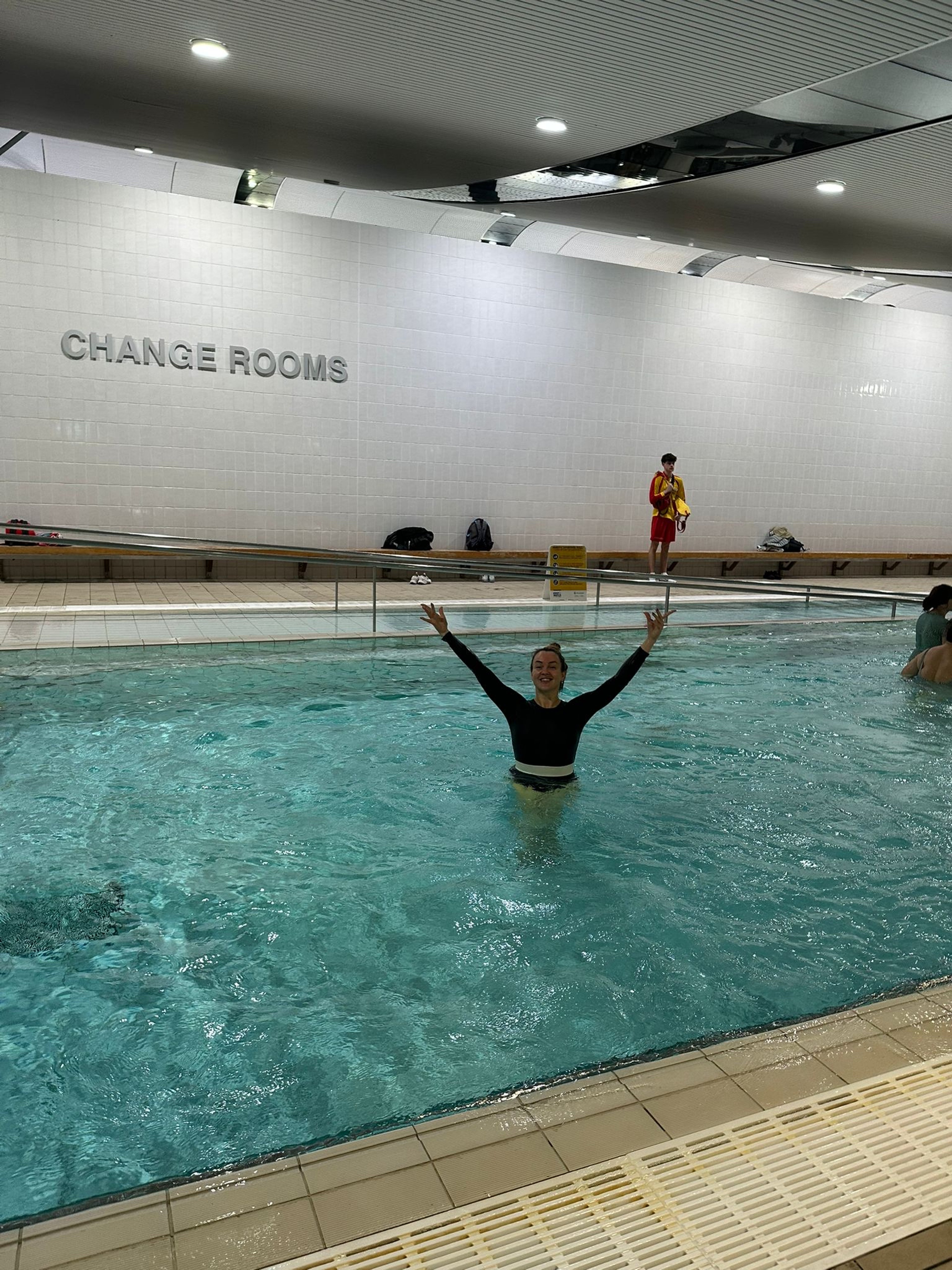 Class participant Morena in the pool with her hands in the air at Ian Thorpe Aquatic Centre 