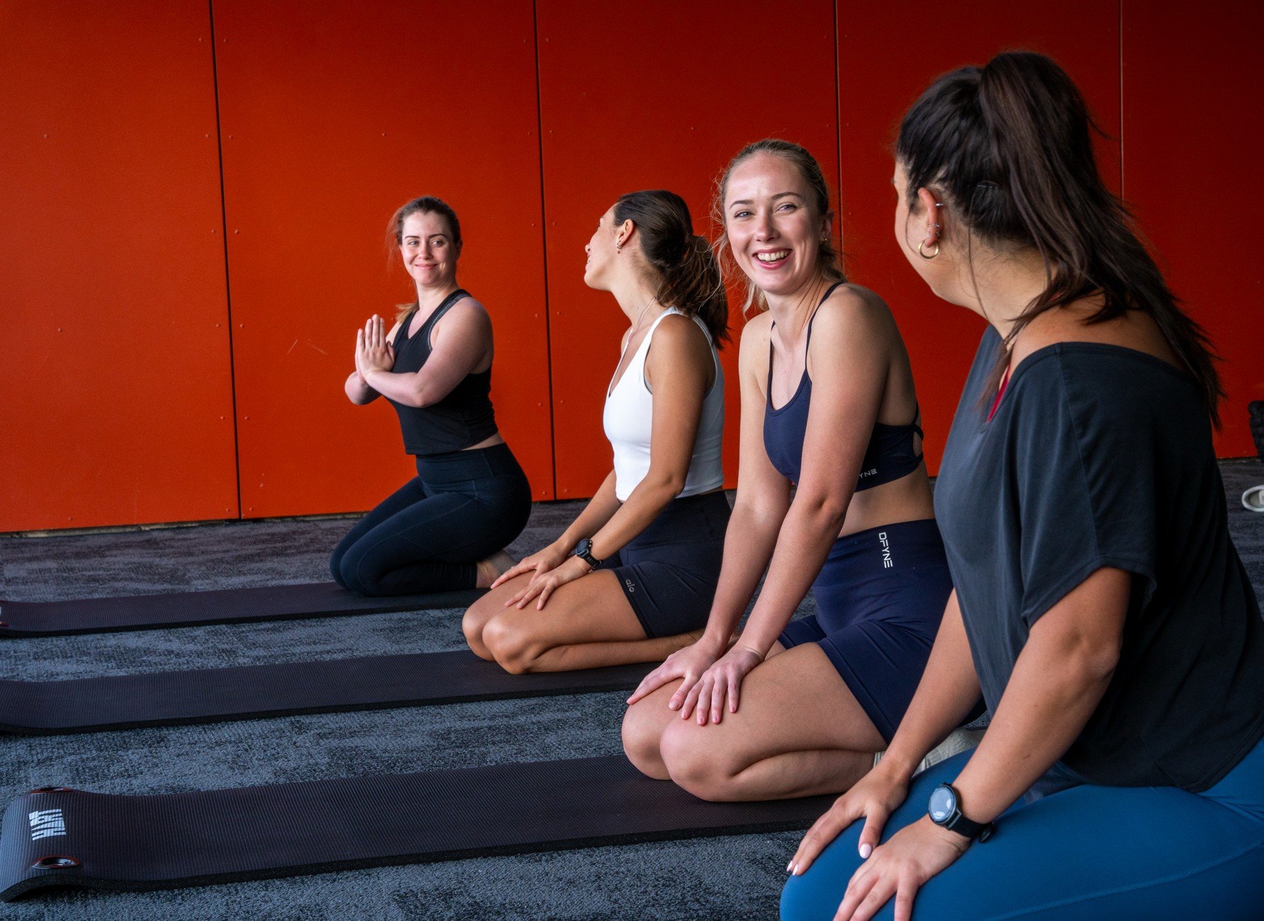 A group of women laughing together on yoga mats in the Charlton Room at Andrew (Boy) Charlton Pool
