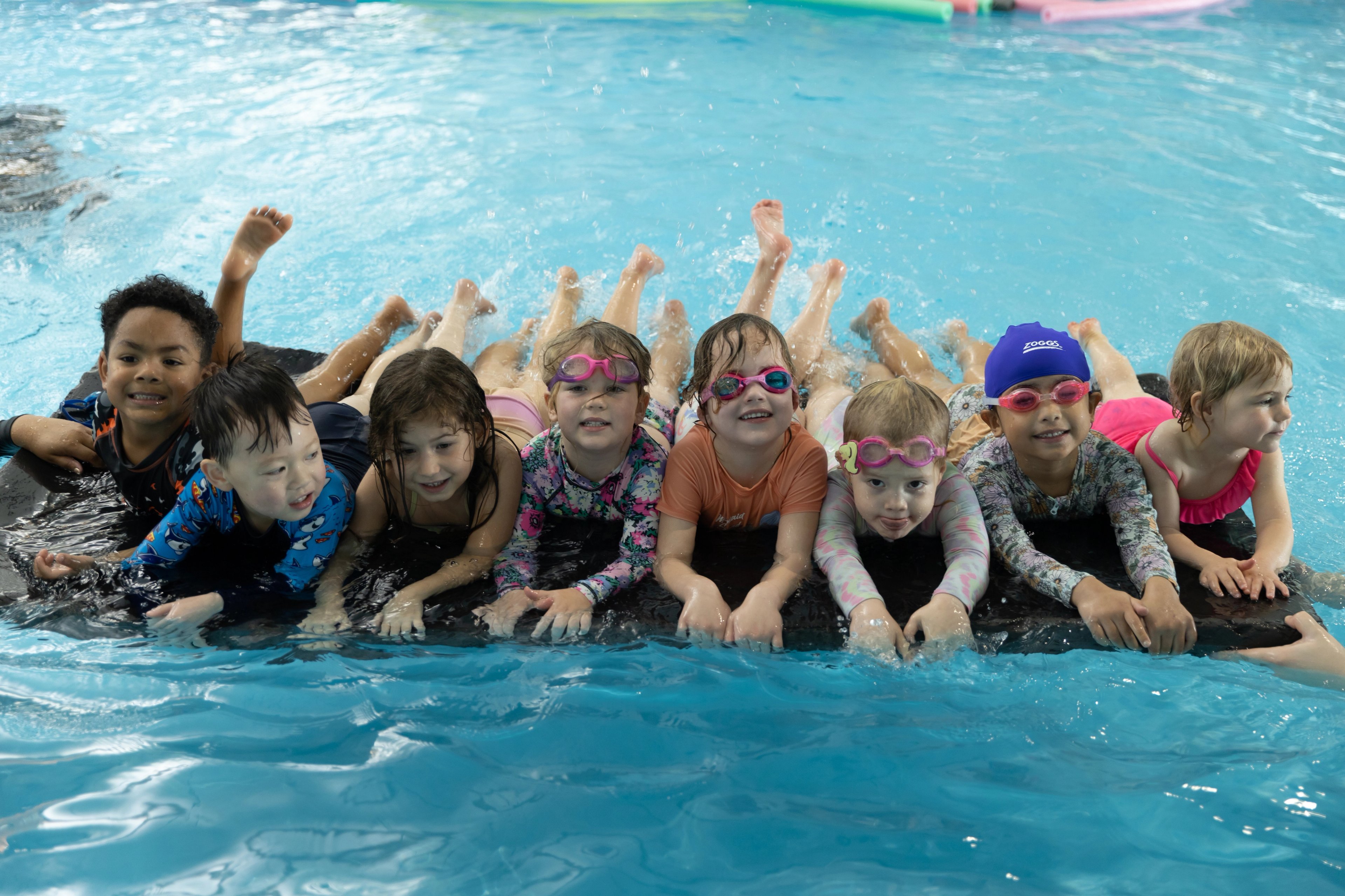 Eight young children lying on a mat in the pool during a swim lesson
