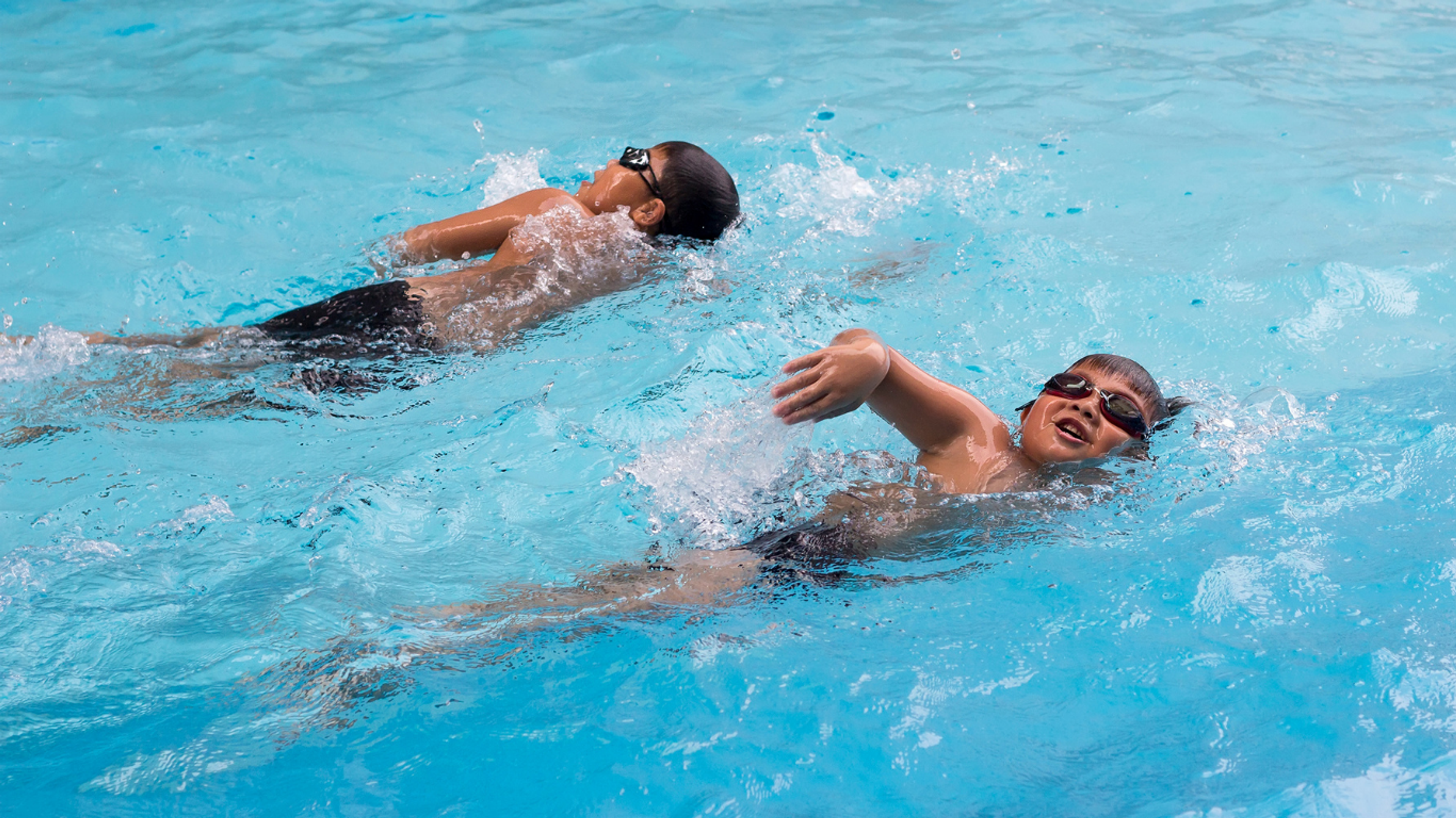 Two young boys doing freestyle laps in the pool