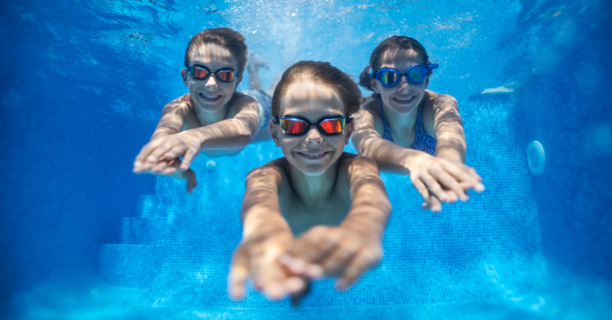 Two kids and a woman diving underneath the water in a pool