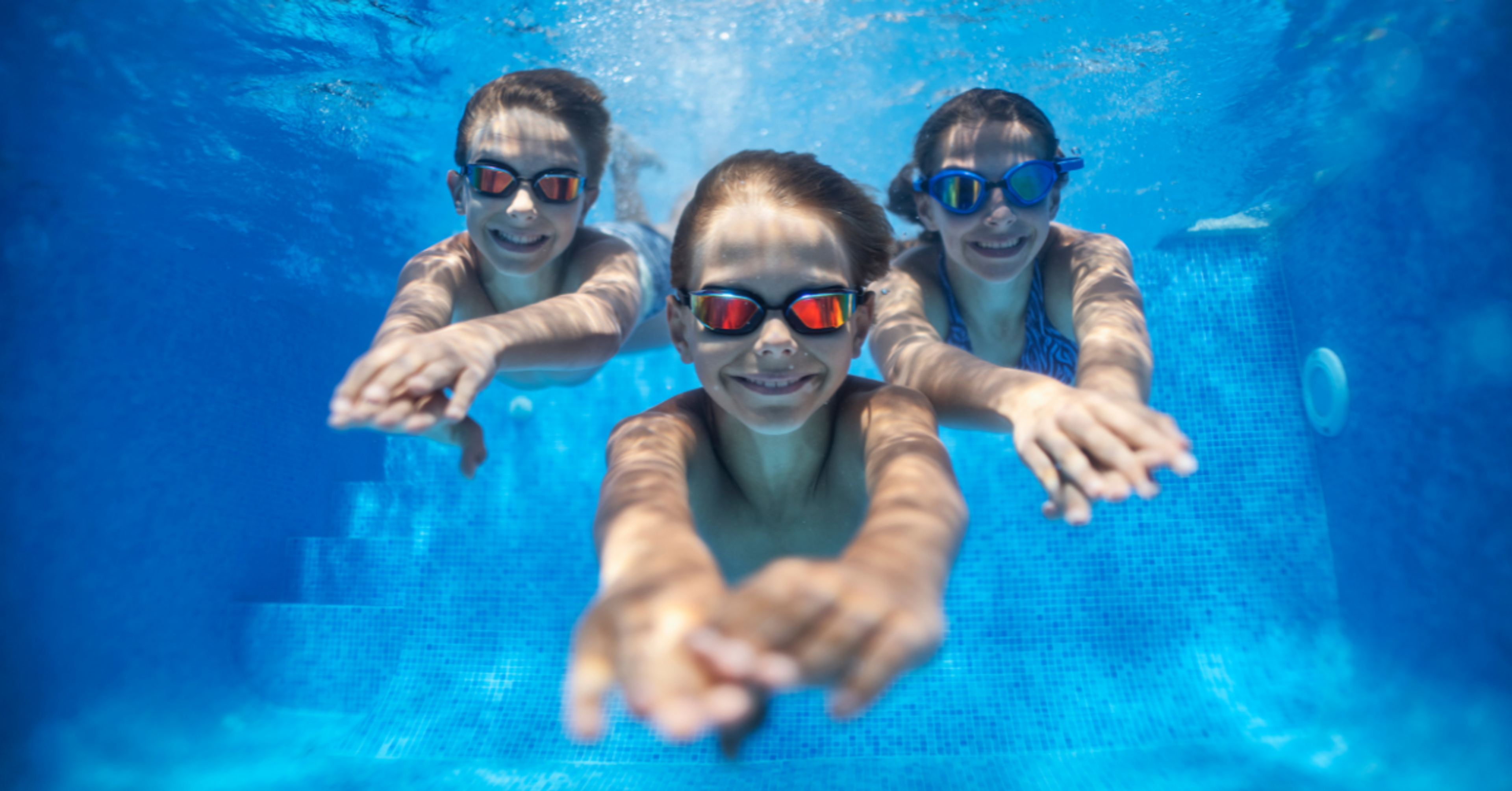 Two kids and a woman diving underneath the water in a pool