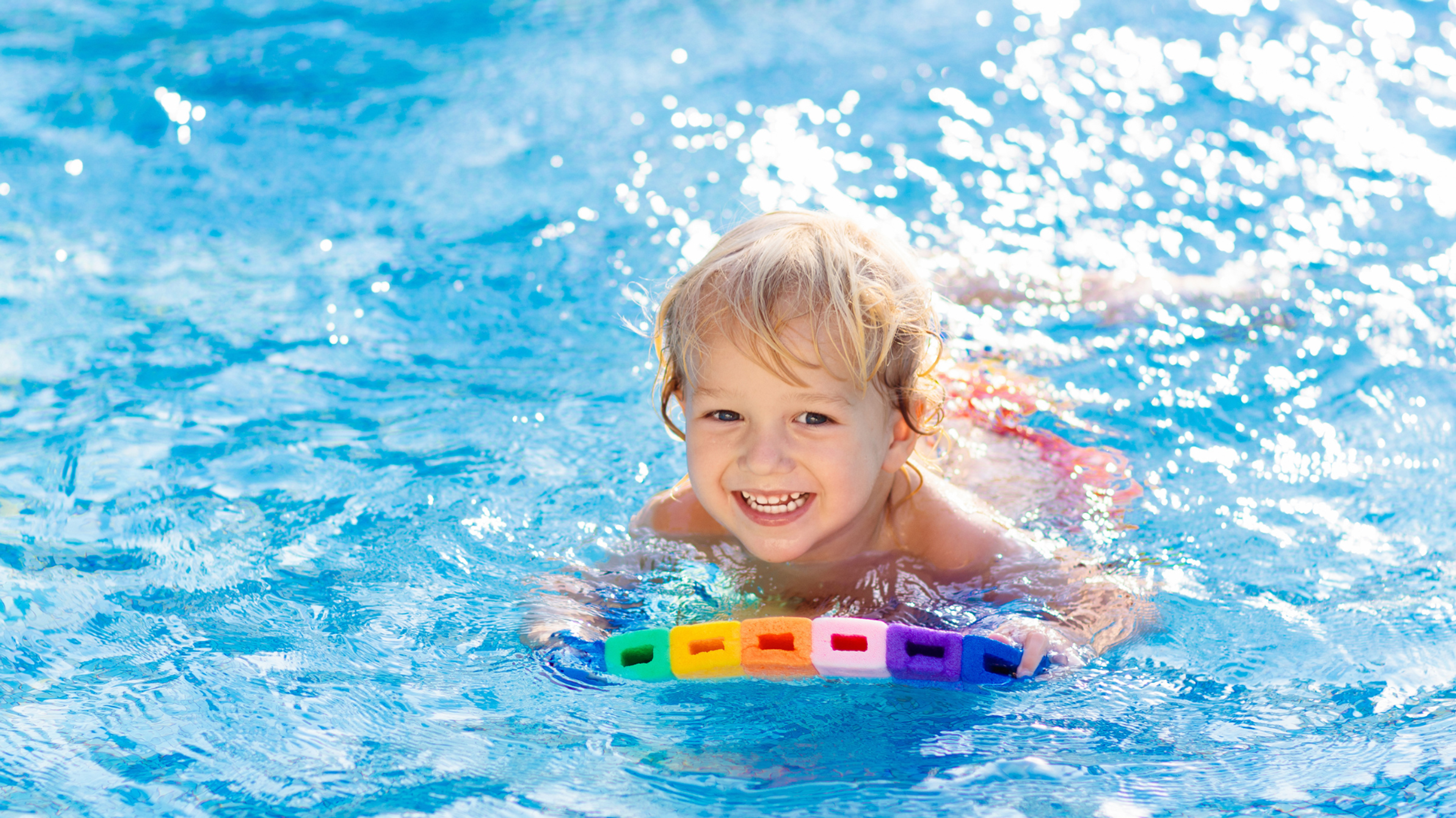 A young child using a colourful flotation device to swim in the pool 